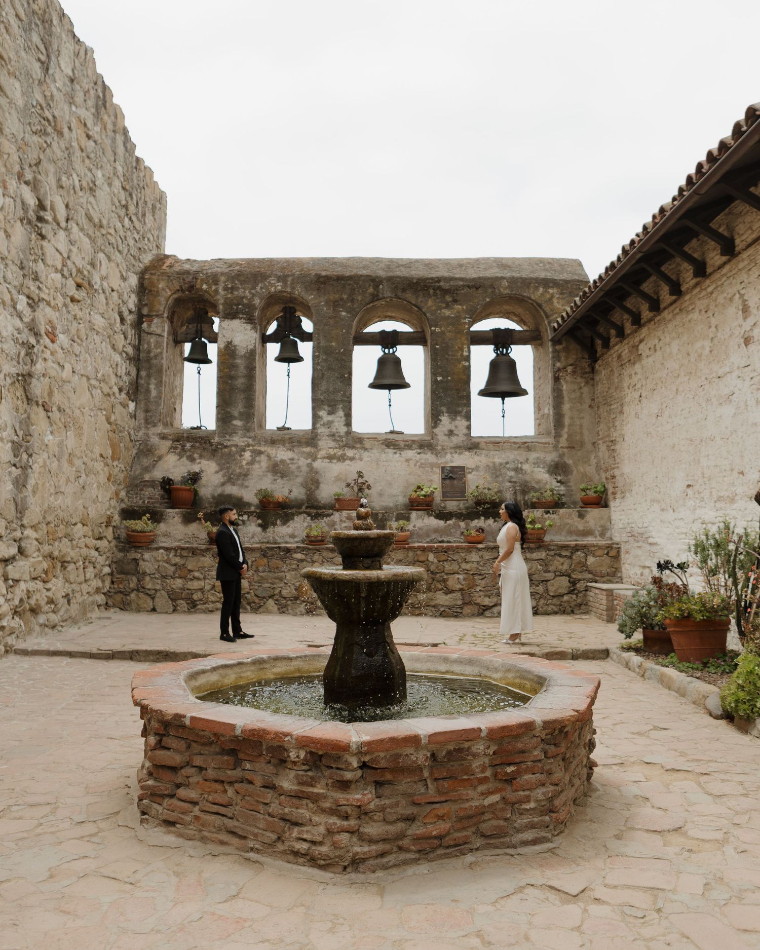 Historic mission courtyard with stone walls and bell tower featuring rustic fountain.