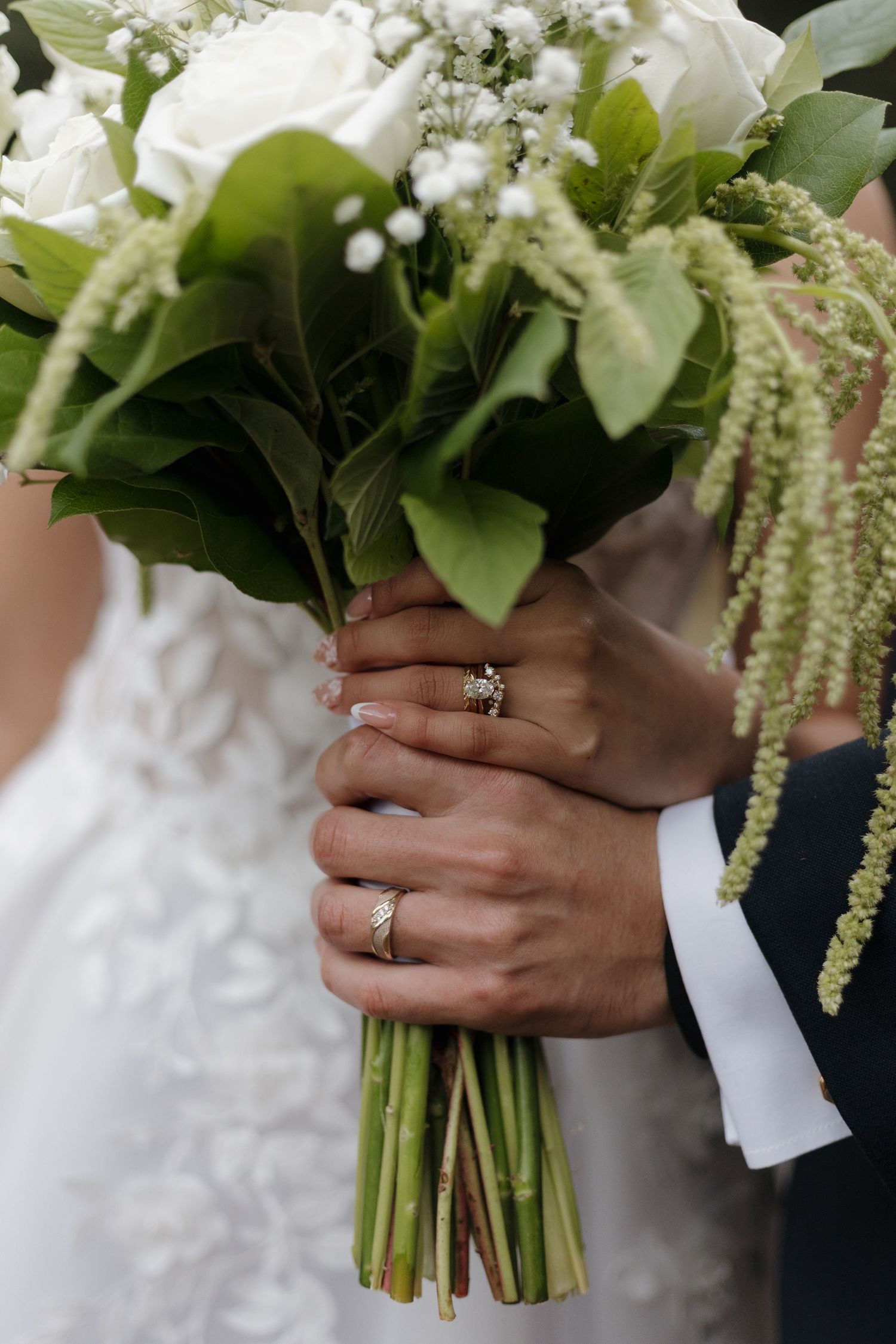 Close-up of hands holding a white wedding bouquet with rings displayed.