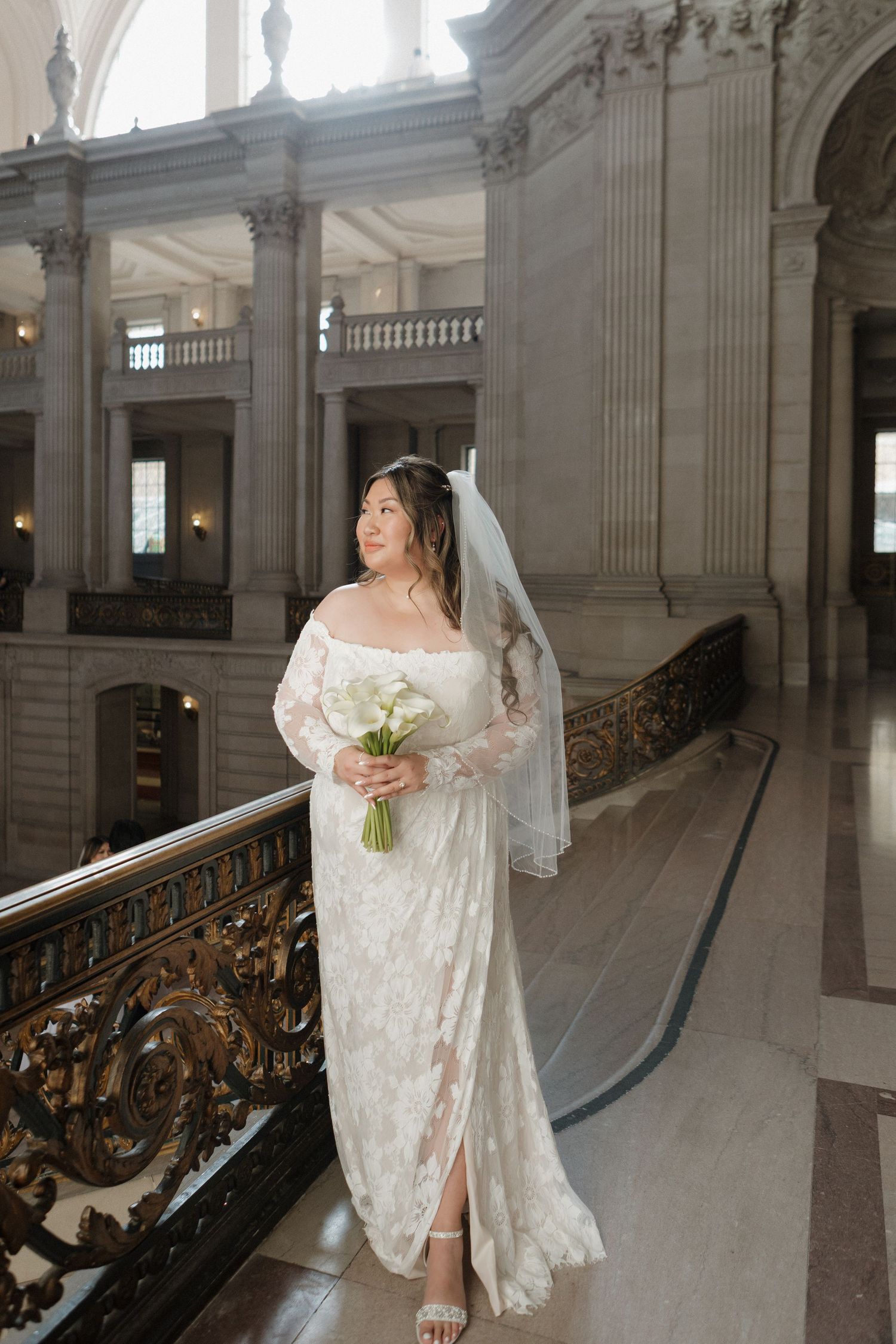 Ornate classical interior with white columns and decorative railings features elegant bridal portrait.
