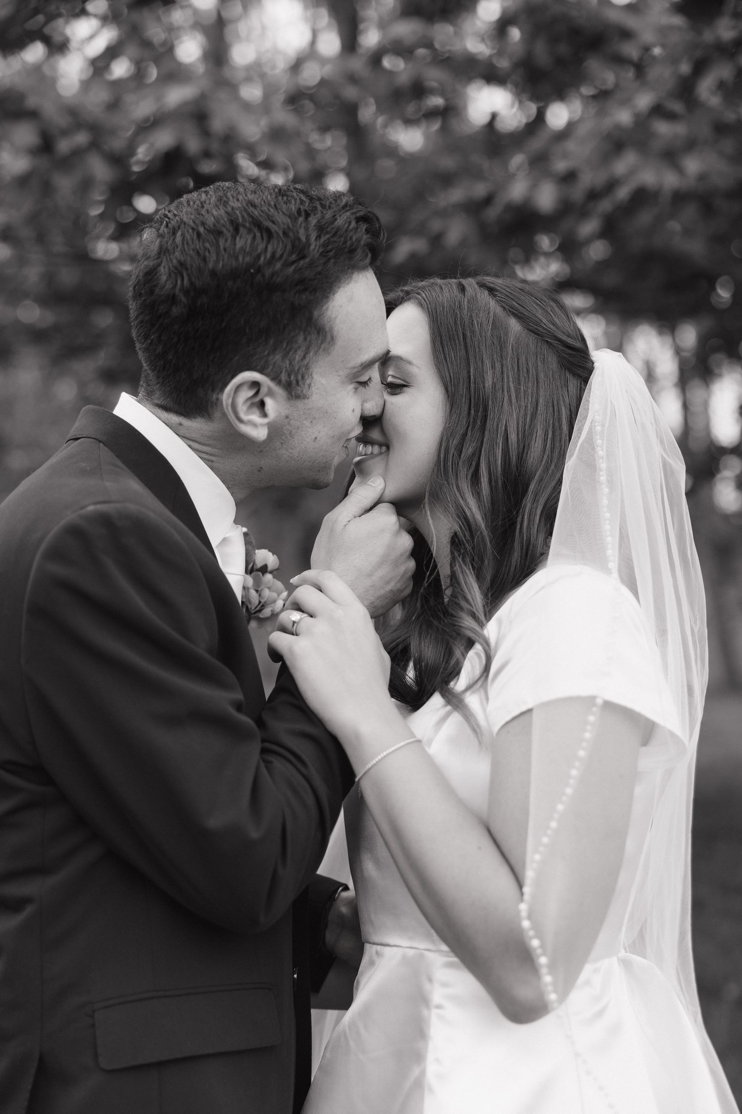 Black and white photo of a bride and groom sharing a tender kiss outdoors on their wedding day.