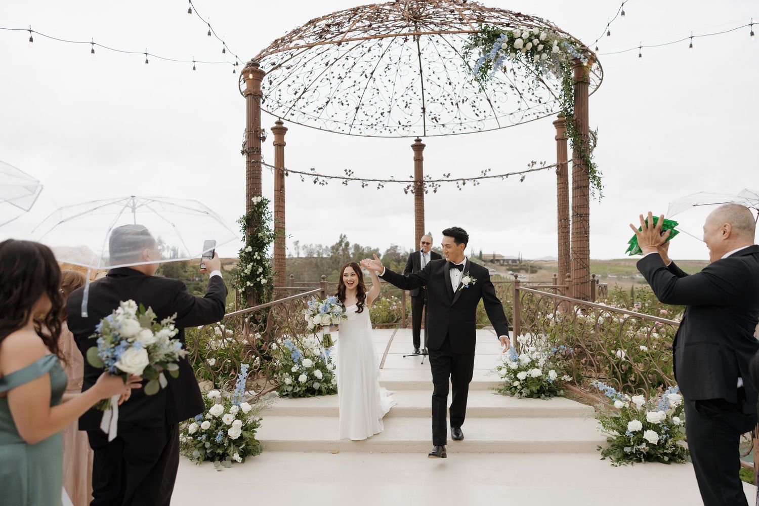 Bride and groom walk down the aisle under a floral gazebo at an elegant outdoor wedding ceremony.