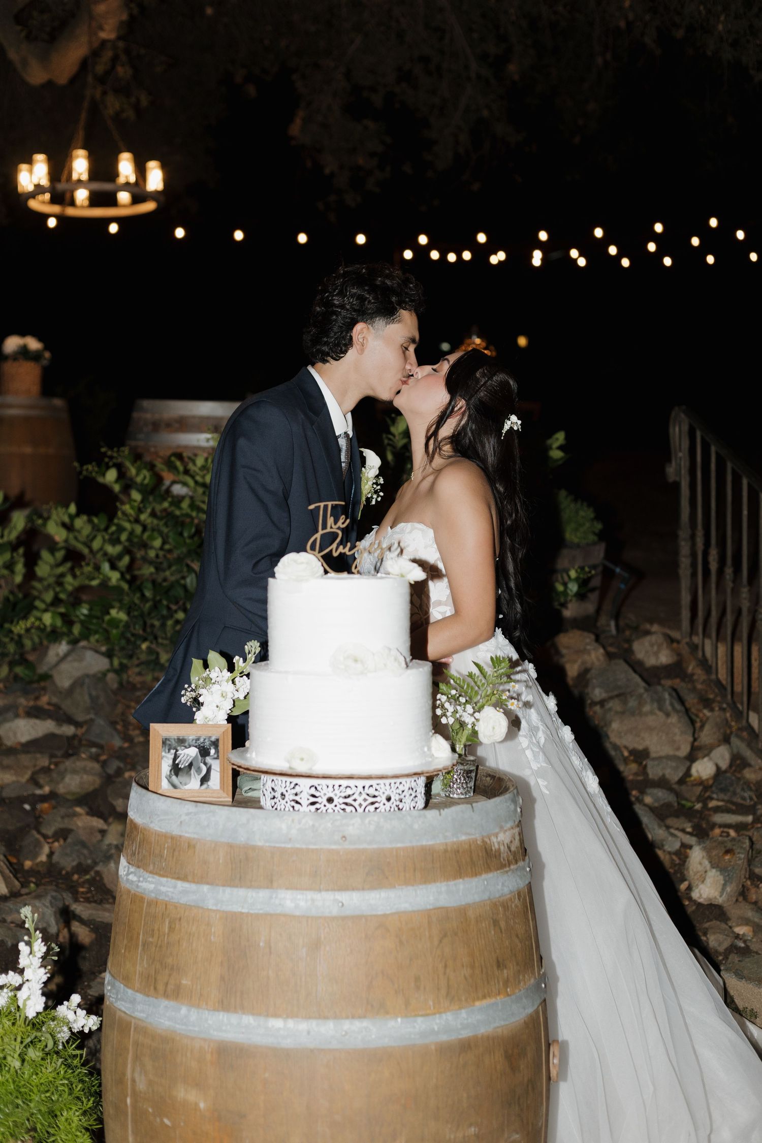 Wedding couple shares an intimate moment behind their wedding cake displayed on a rustic wine barrel.