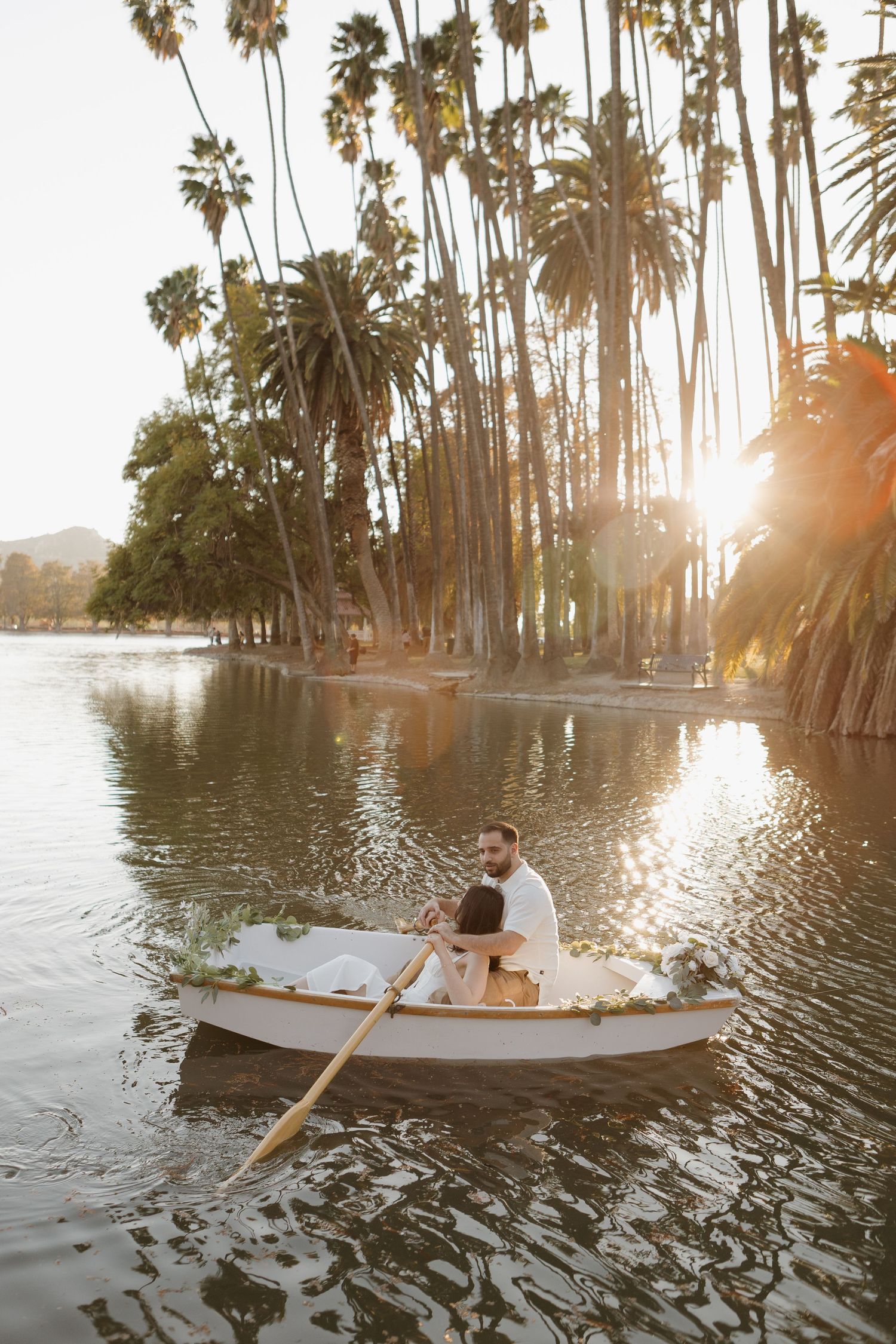 Romantic rowboat scene on a lake surrounded by palm trees at sunset.