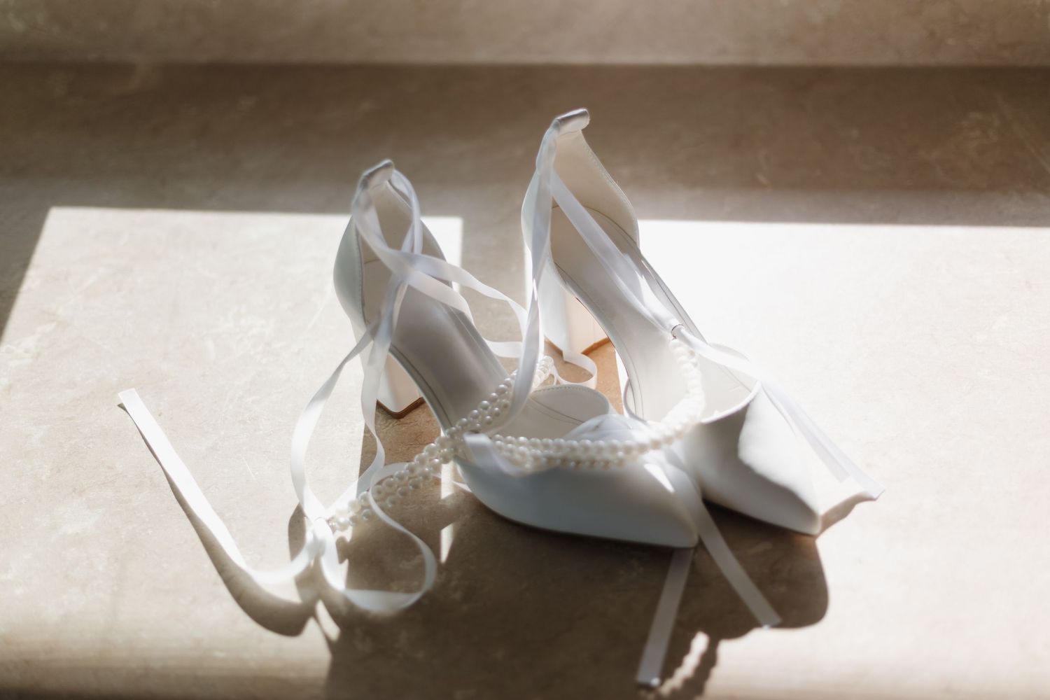 Elegant white bridal shoes photographed in natural window light.