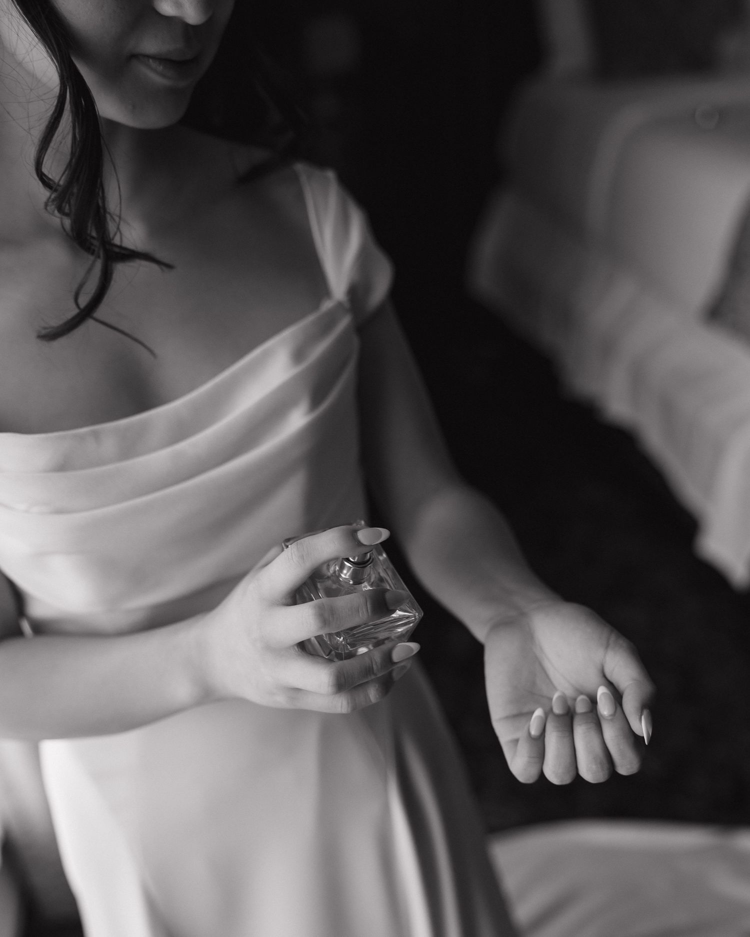 Black and white photo of a bride in white dress applying perfume to her wrist while getting ready.