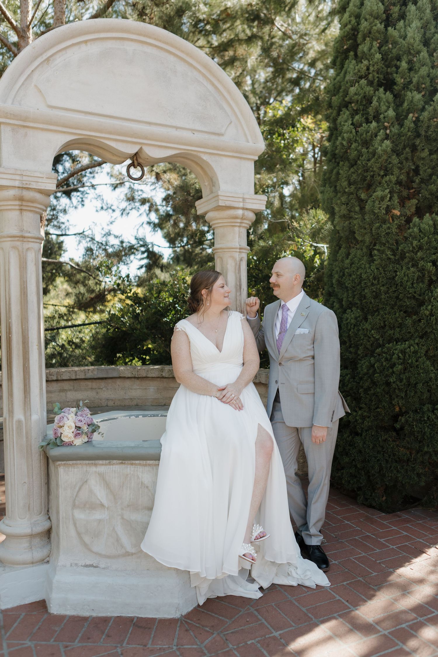 Wedding couple posing under elegant stone archways in a garden setting.
