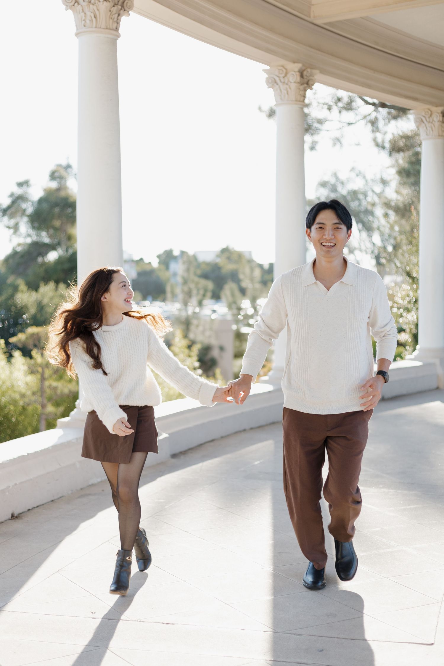 Playful couple dances and spins under white columns in bright sunlight.