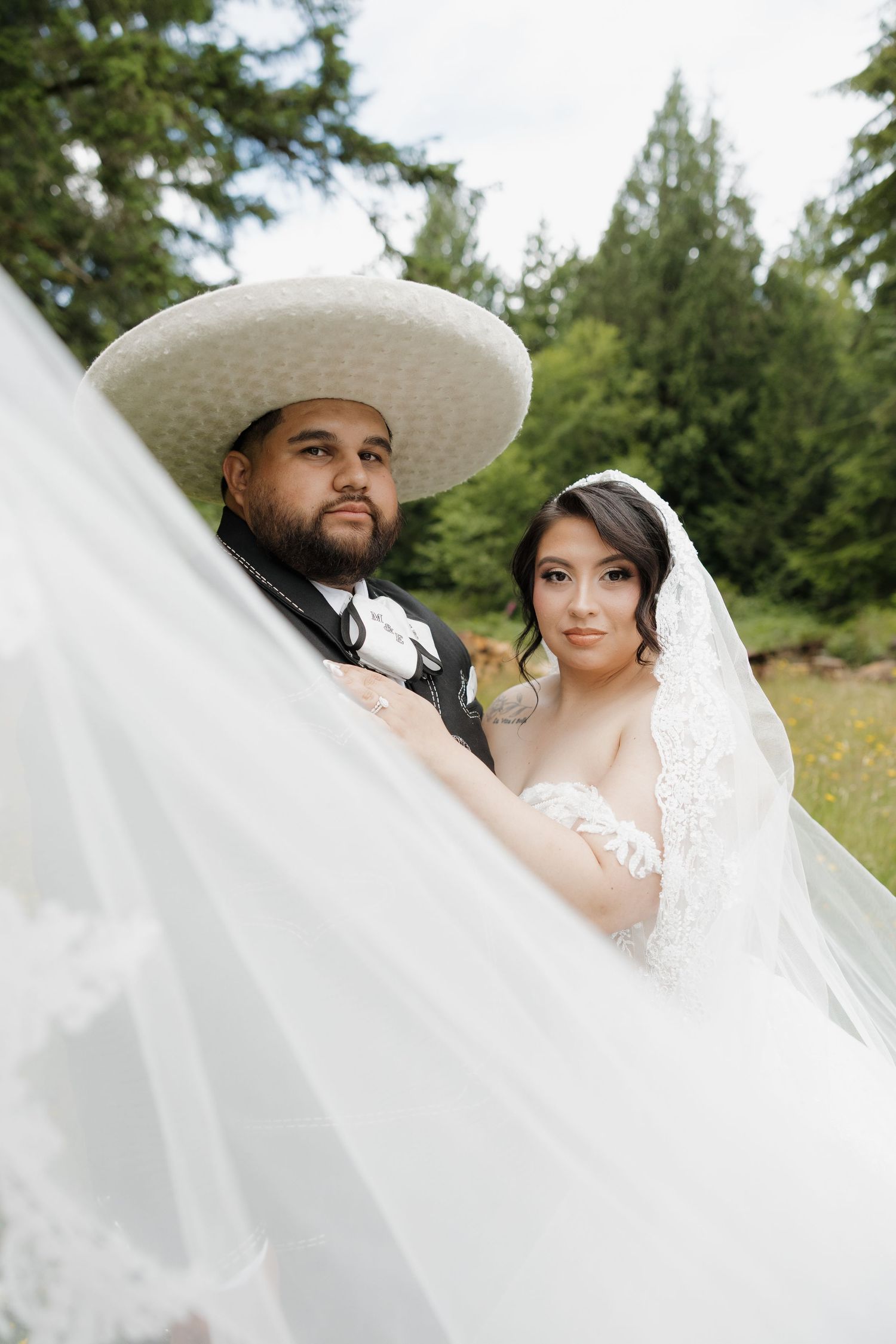 groom in a wide-brim hat and bride in a lace veil pose together outdoors among tall evergreen trees. Seattle, Washington Wedding Photography