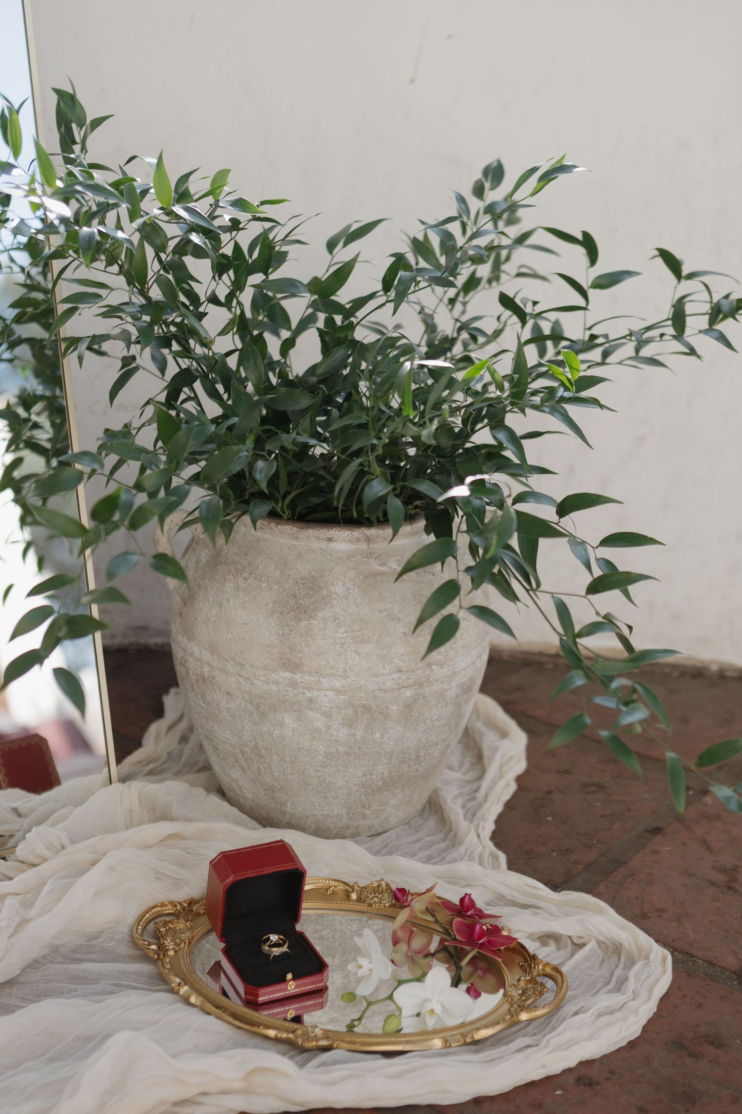 Wedding details with greenery, ring box, and decor arranged on white fabric.