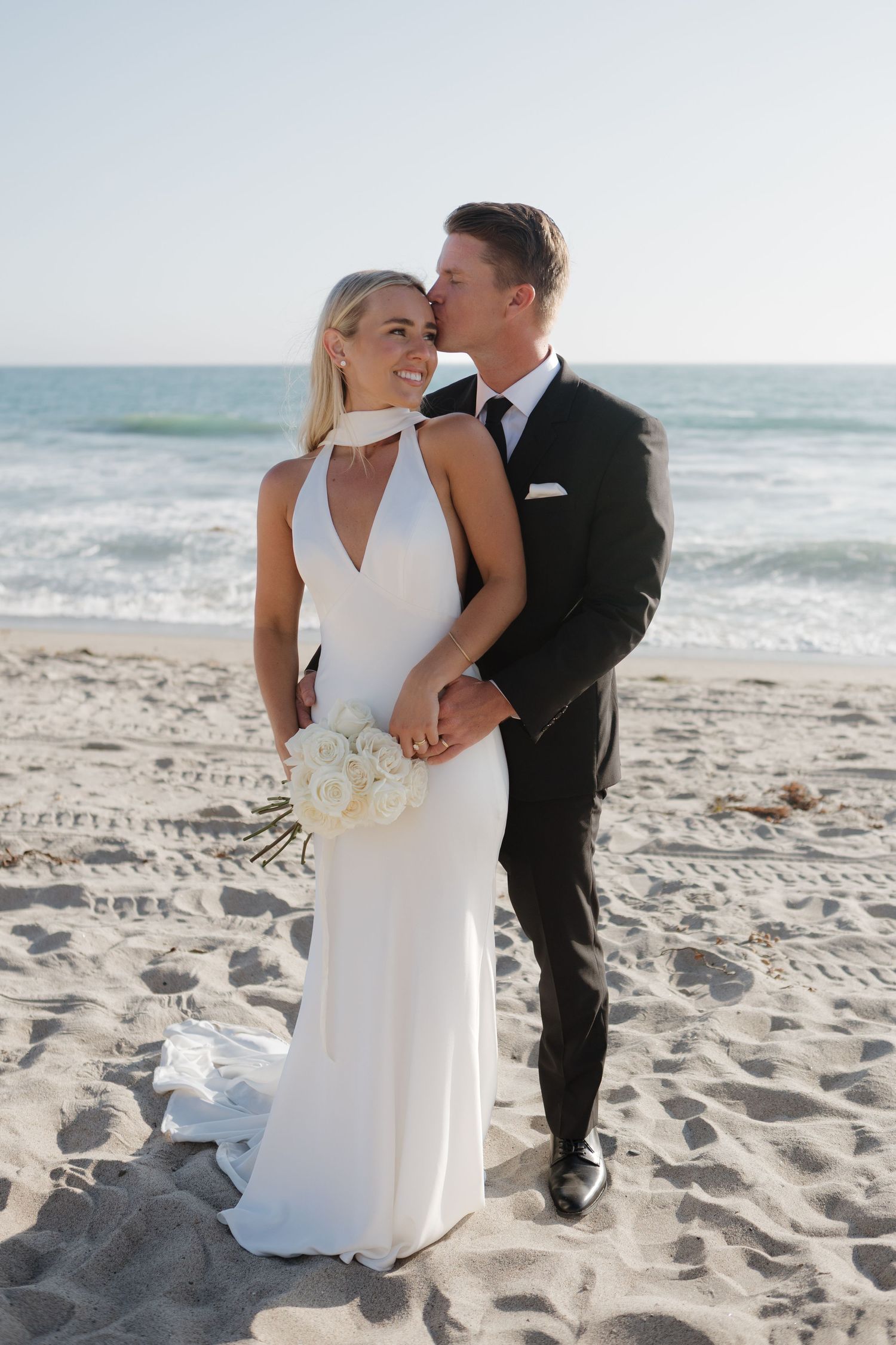 A beach wedding portrait with couple in formal attire standing on sandy shore.