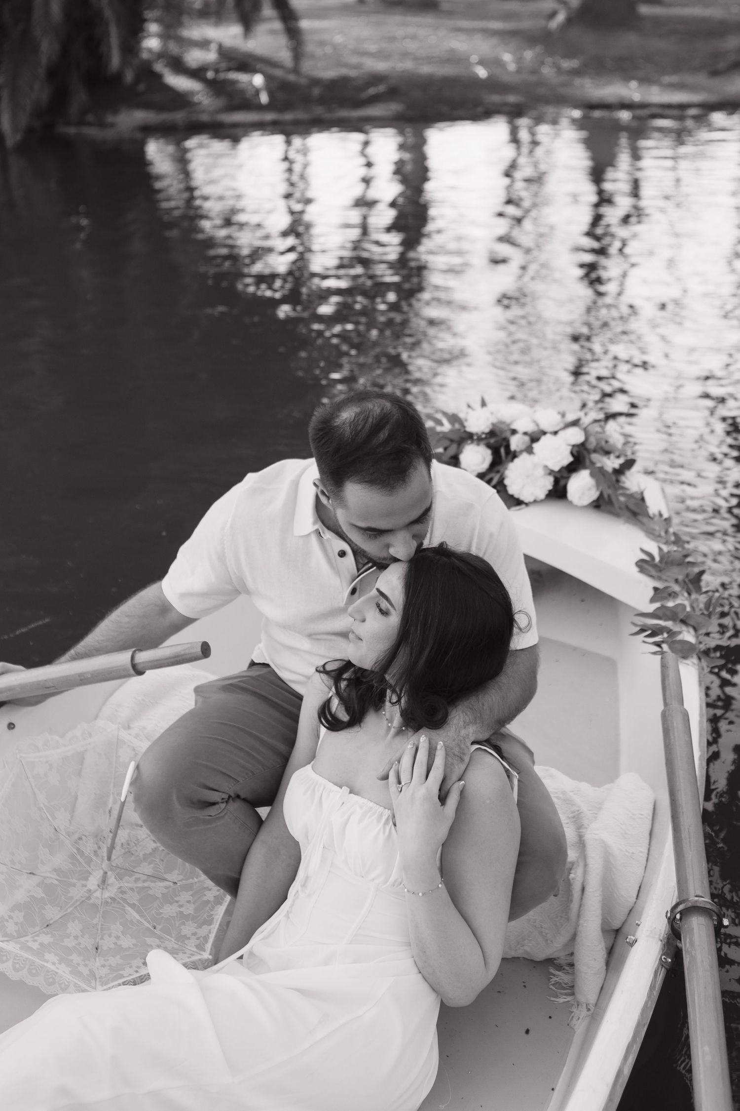 Couple sharing an intimate moment in a white rowboat on calm waters.