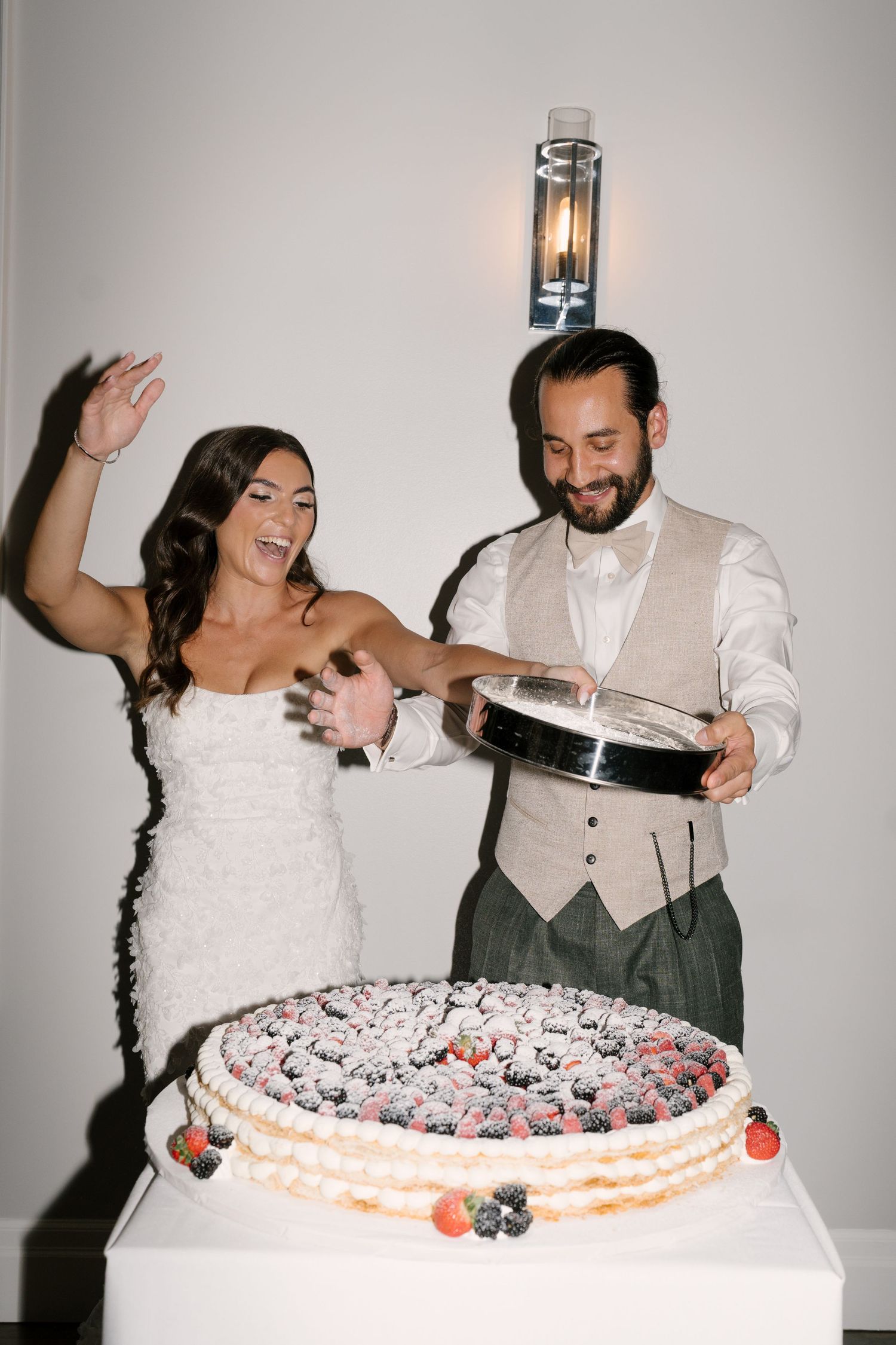 Smiling bride and groom cut a large berry-topped wedding cake during their reception celebration.