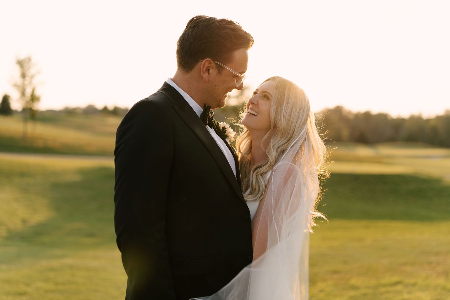 Bride and groom smiling at each other in golden sunset light on a Whistle Bear golf course.