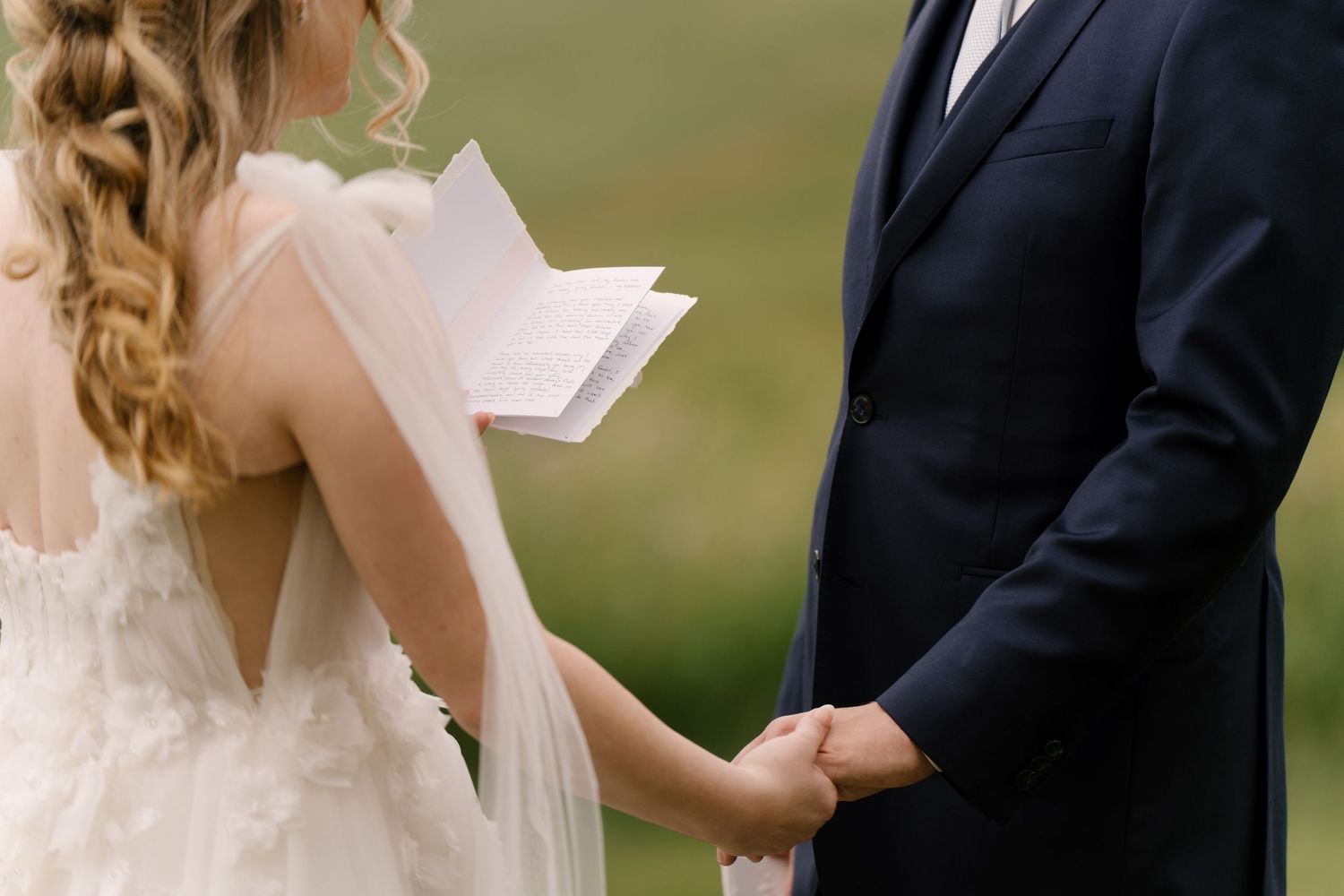 Bride reads vows from paper while holding grooms hands during outdoor wedding ceremony at St Marys Golf Club.