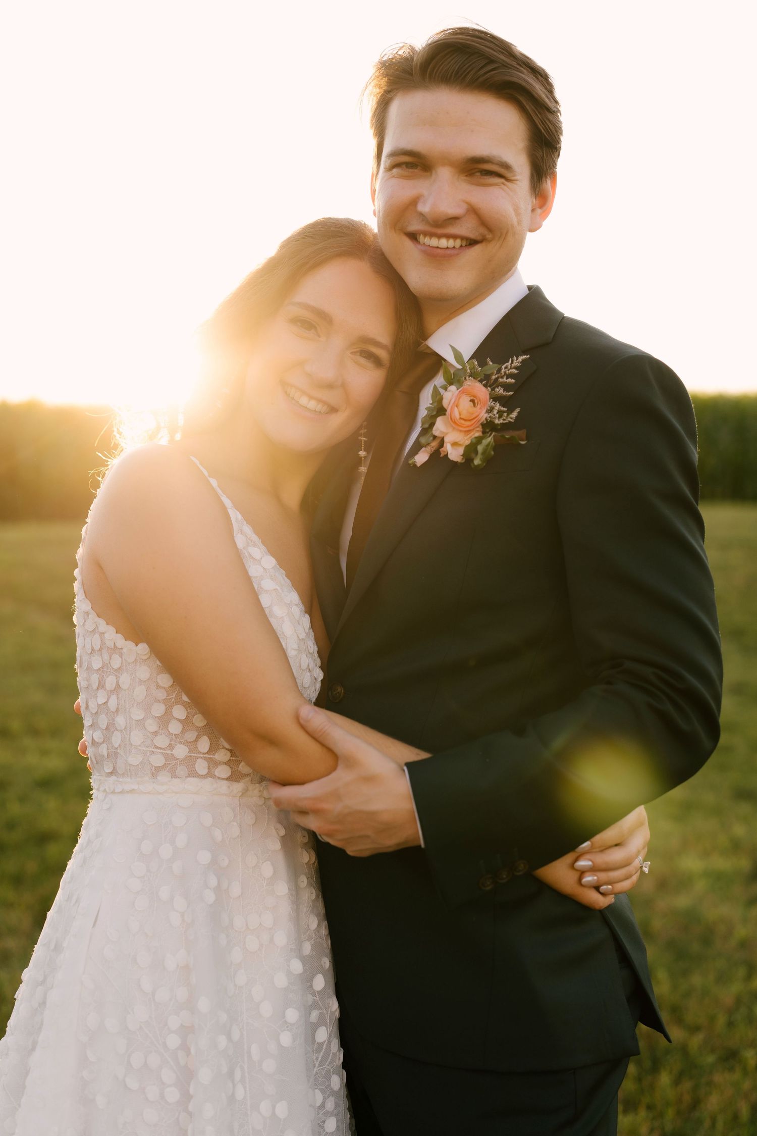 Smiling bride and groom embracing in warm golden sunset light in an open green Wakefield Estates field.