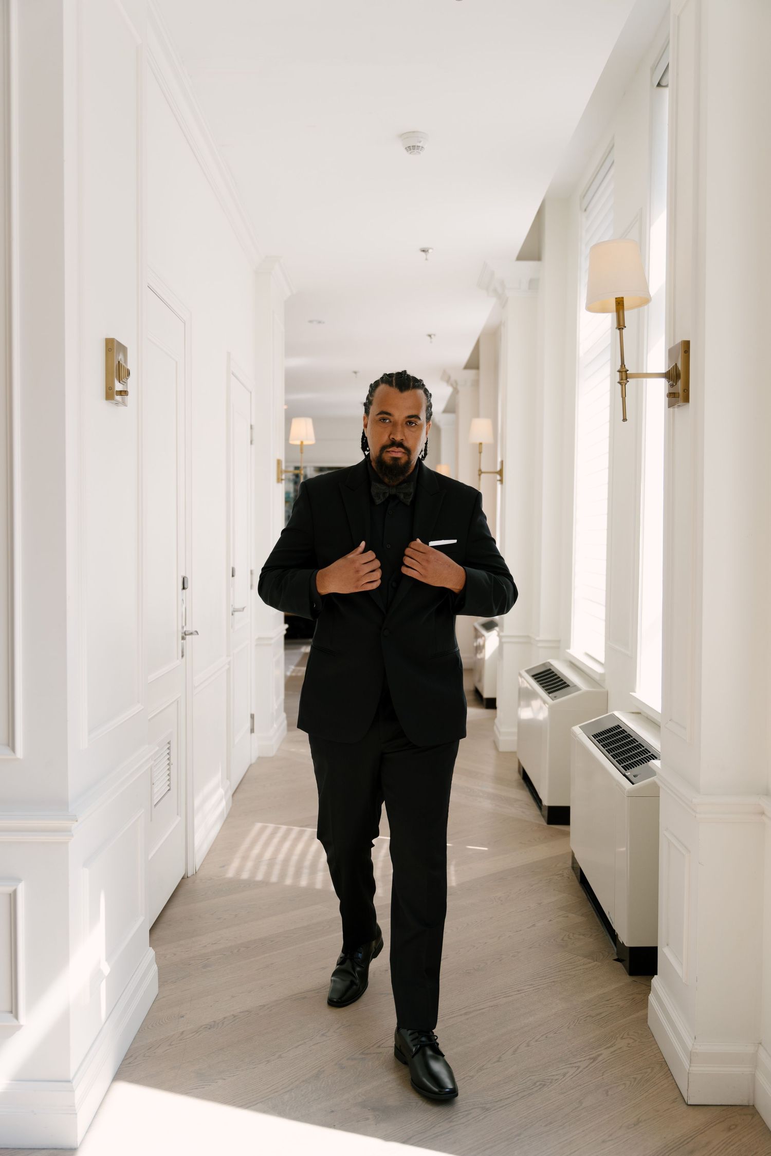 Elegant man in black tuxedo walking through a bright white hotel corridor at The Walper Hotel.
