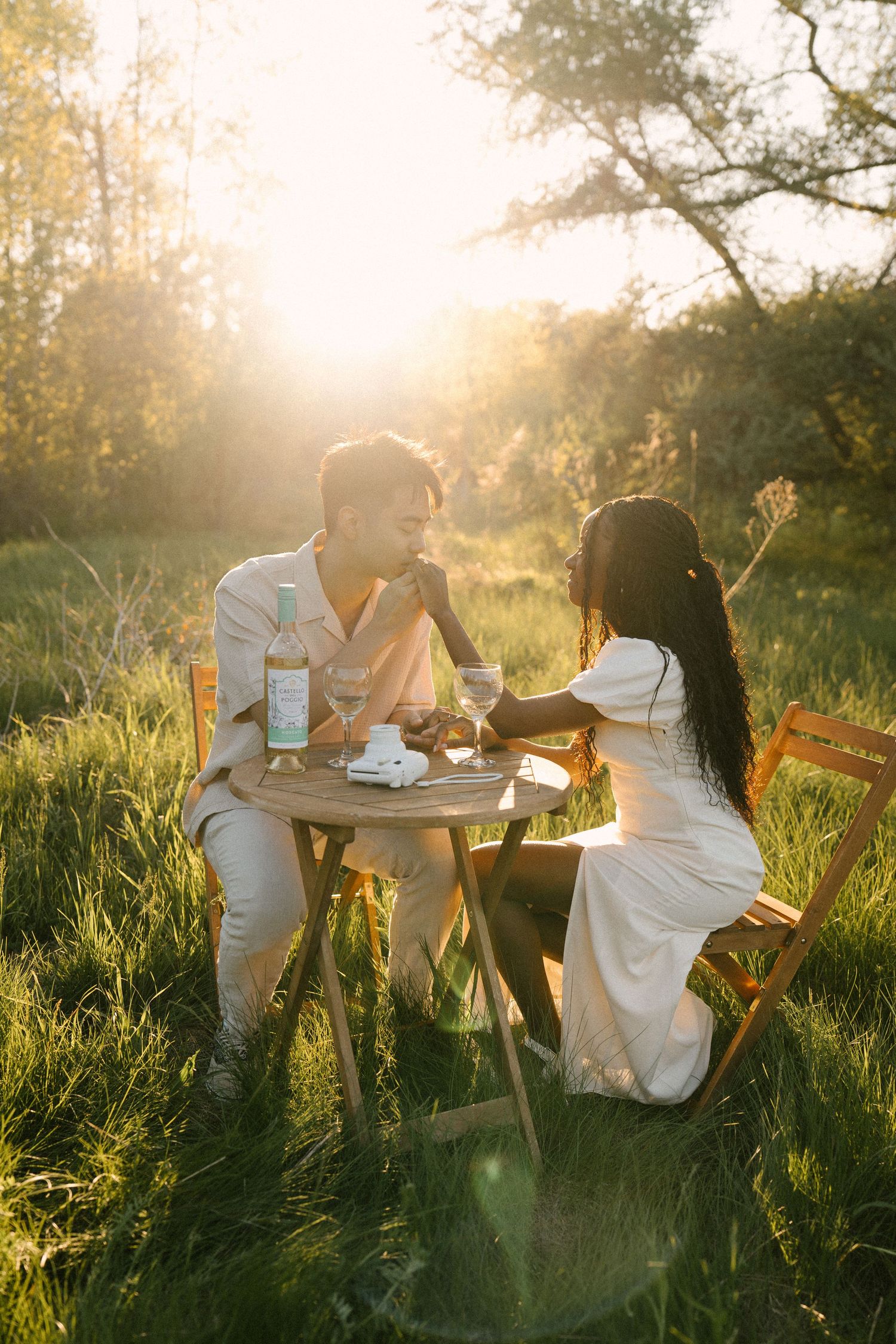 Romantic couple holding hands at outdoor table in glowing golden hour light.