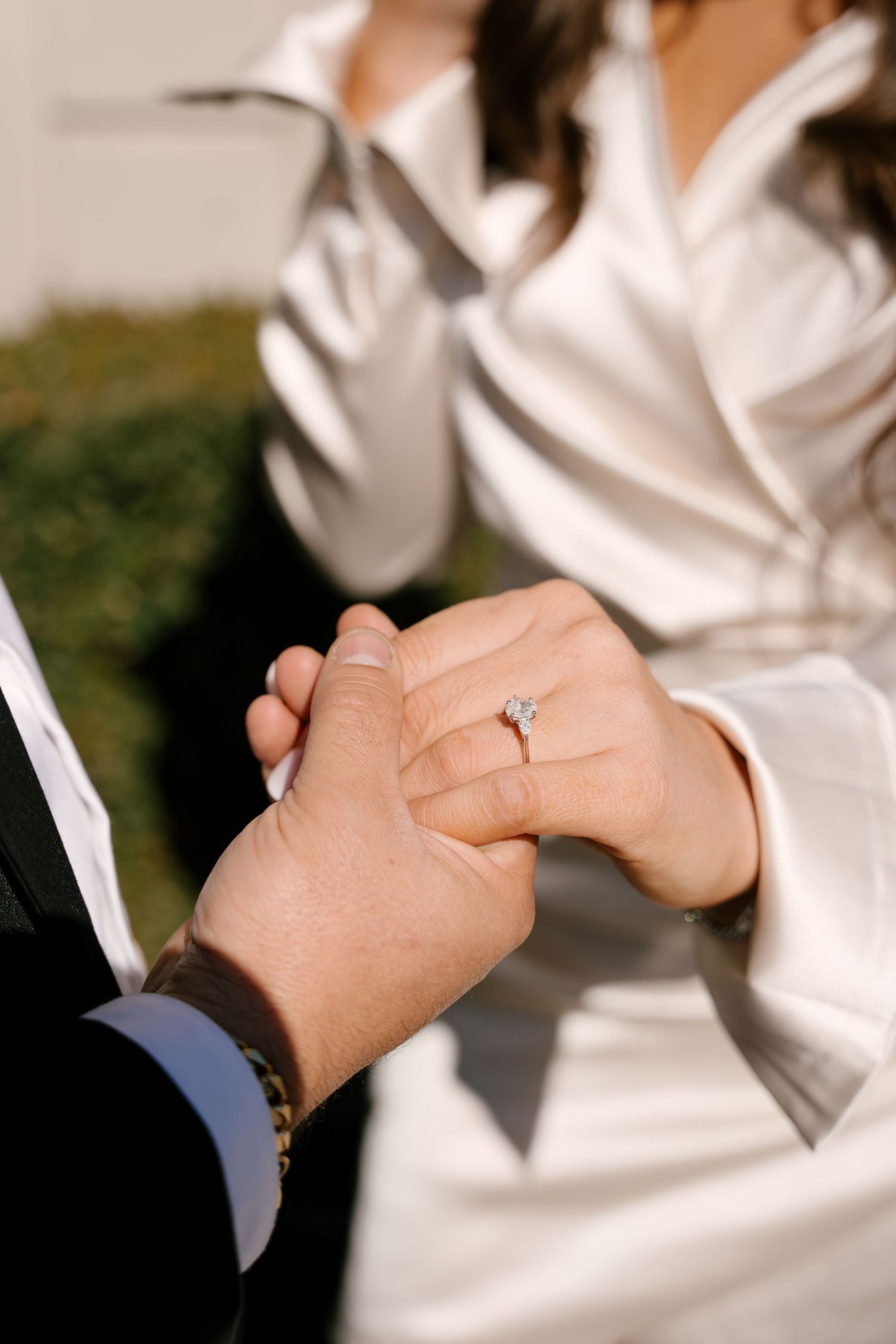 Close-up of engaged couple holding hands showing diamond engagement ring in sunlight.