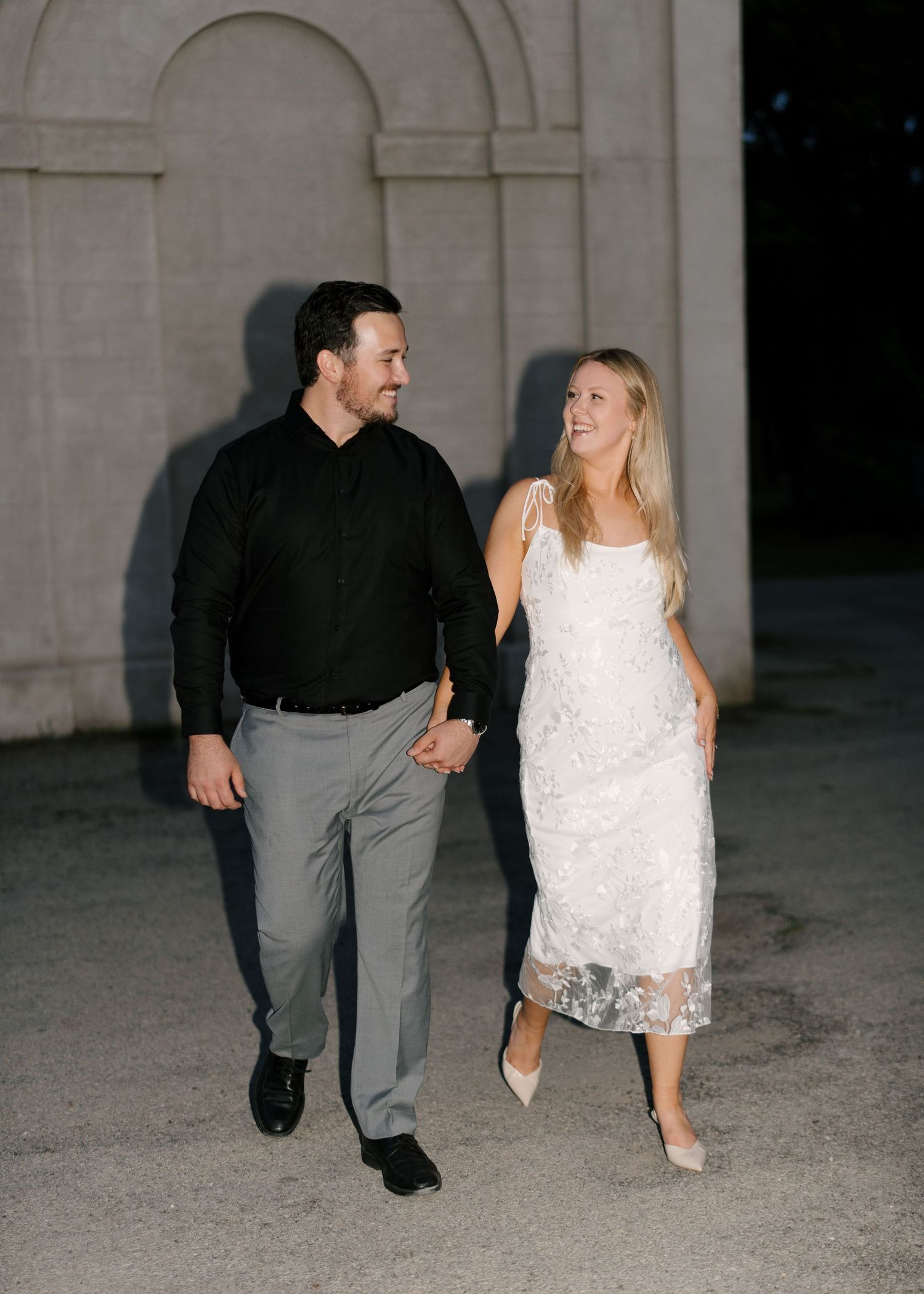 Happy couple in black and white outfits laughing while strolling together at night outdoors.