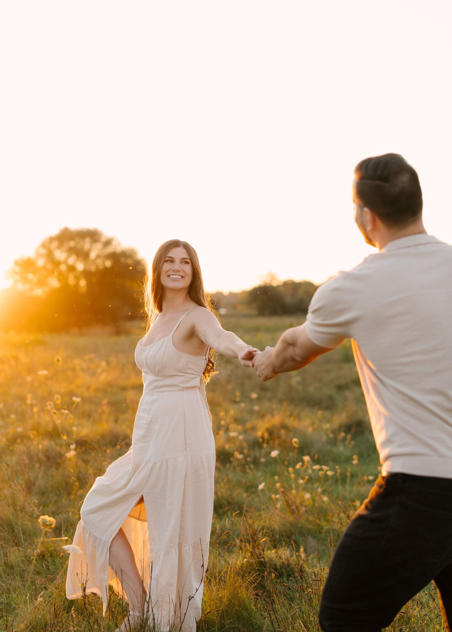 Joyful couple holding hands and spinning together in a wildflower meadow at sunset.