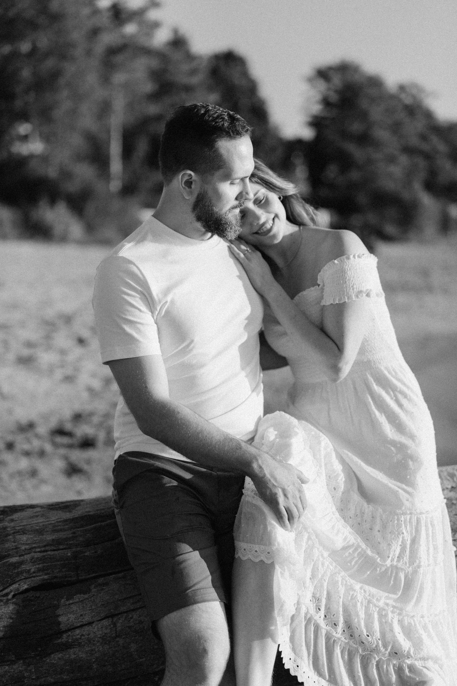 Black and white photo of couple sitting together on a log in a natural setting.