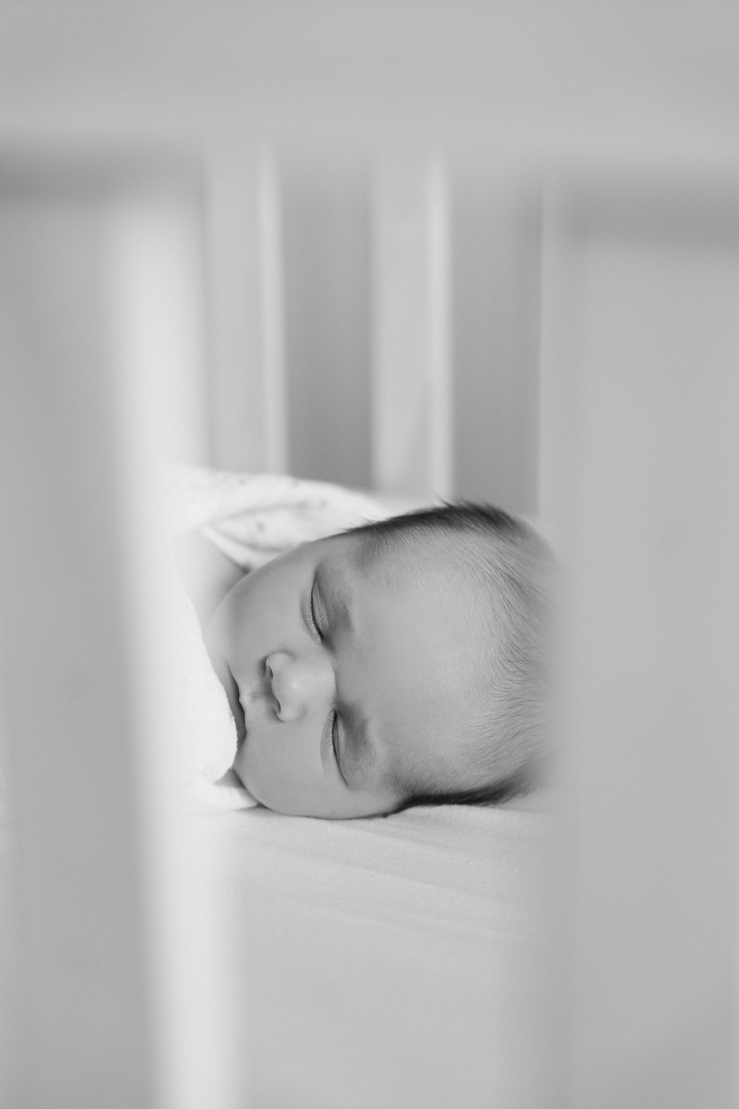 Black and white close-up of peaceful sleeping newborn baby lying in white crib.