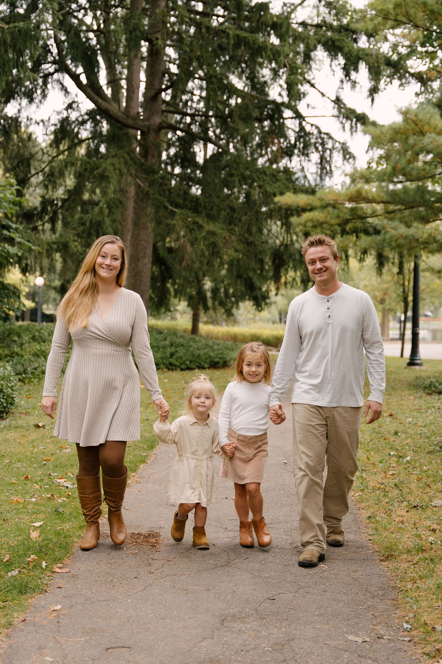 Young family of four walking on park path, two toddler girls holding parents hands.