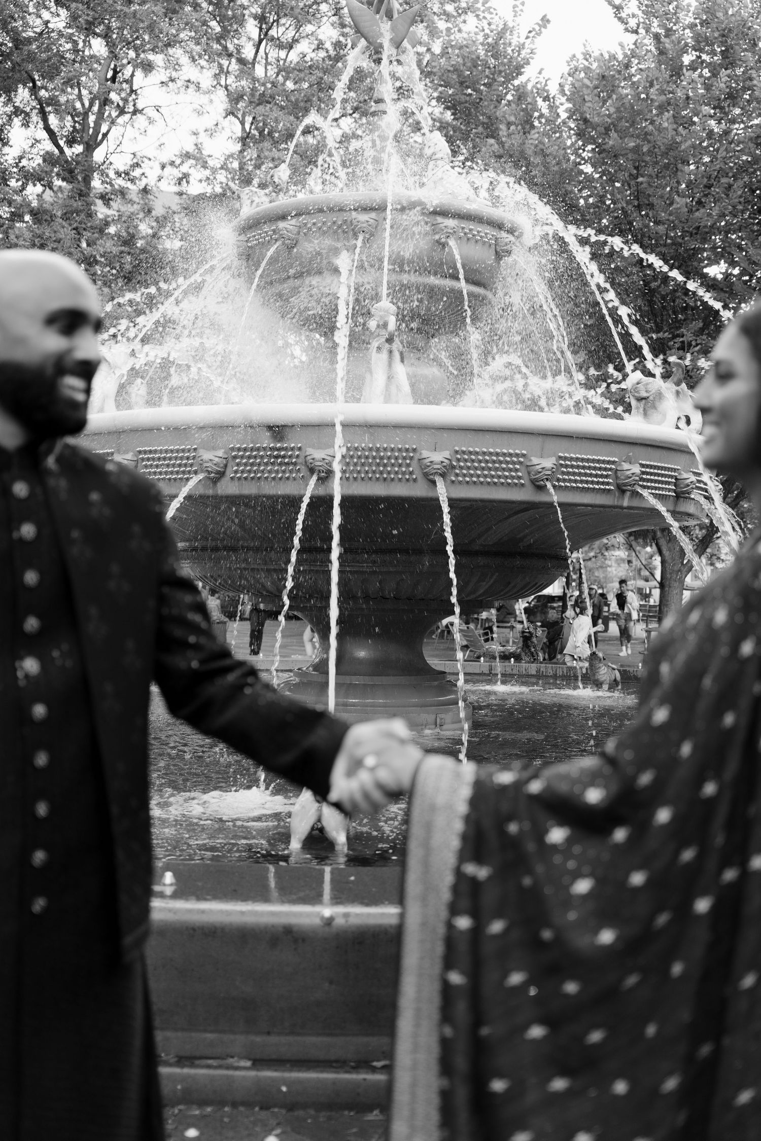 Couple in traditional South Asian attire holding hands in front of a fountain in black and white in Toronto.