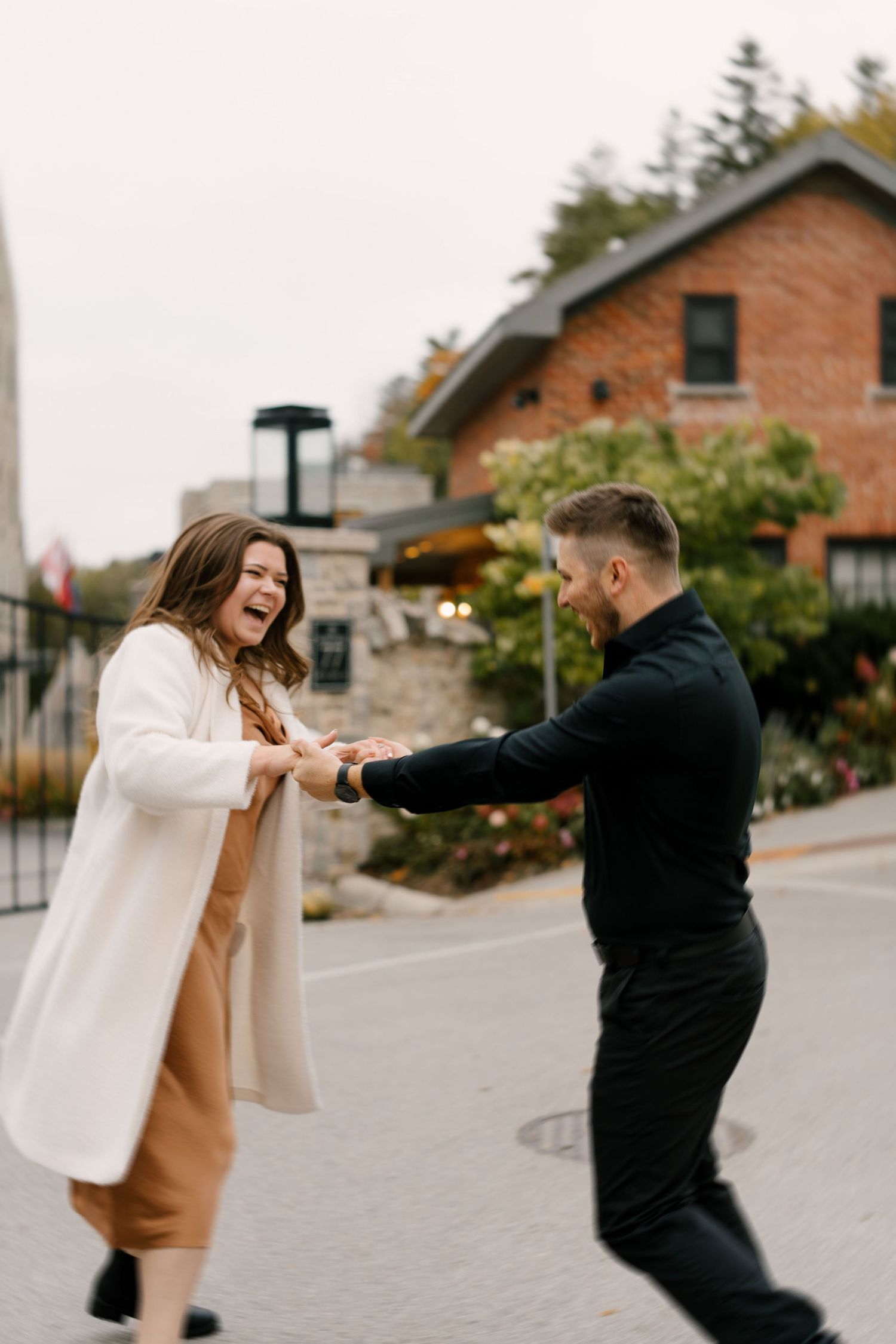 Laughing couple dancing and spinning together on a cobblestone street with a brick building backdrop.