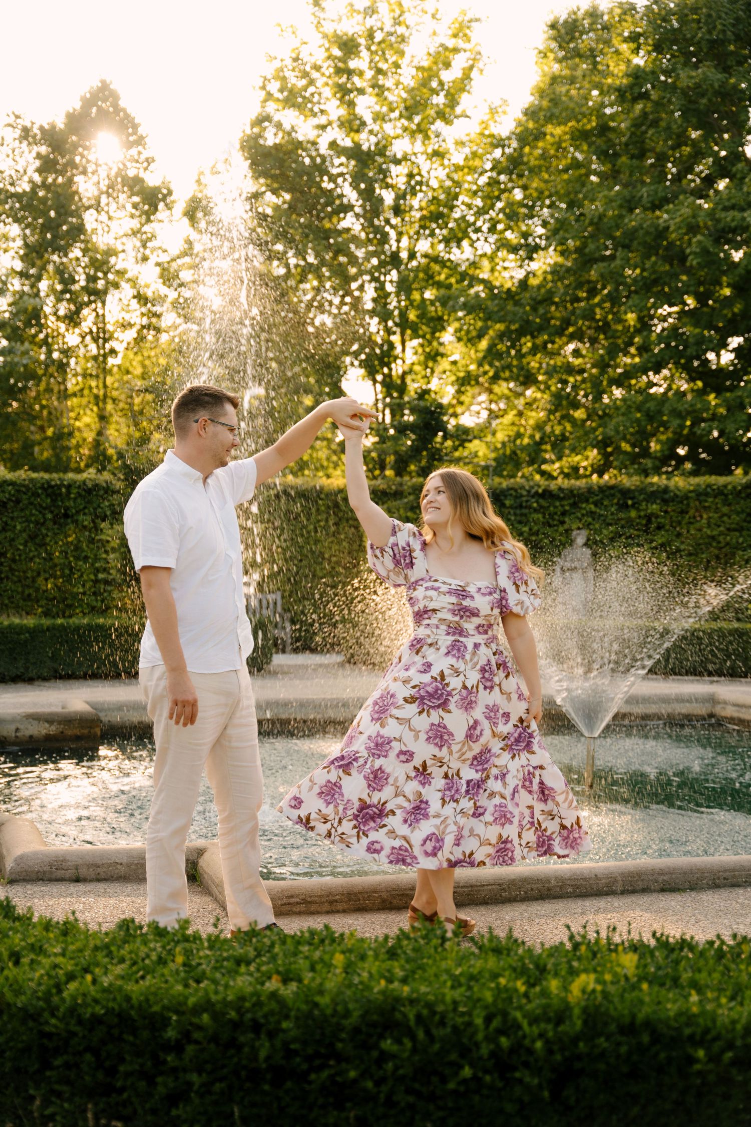 Couple dancing and toasting near a garden fountain surrounded by lush greenery at golden hour.