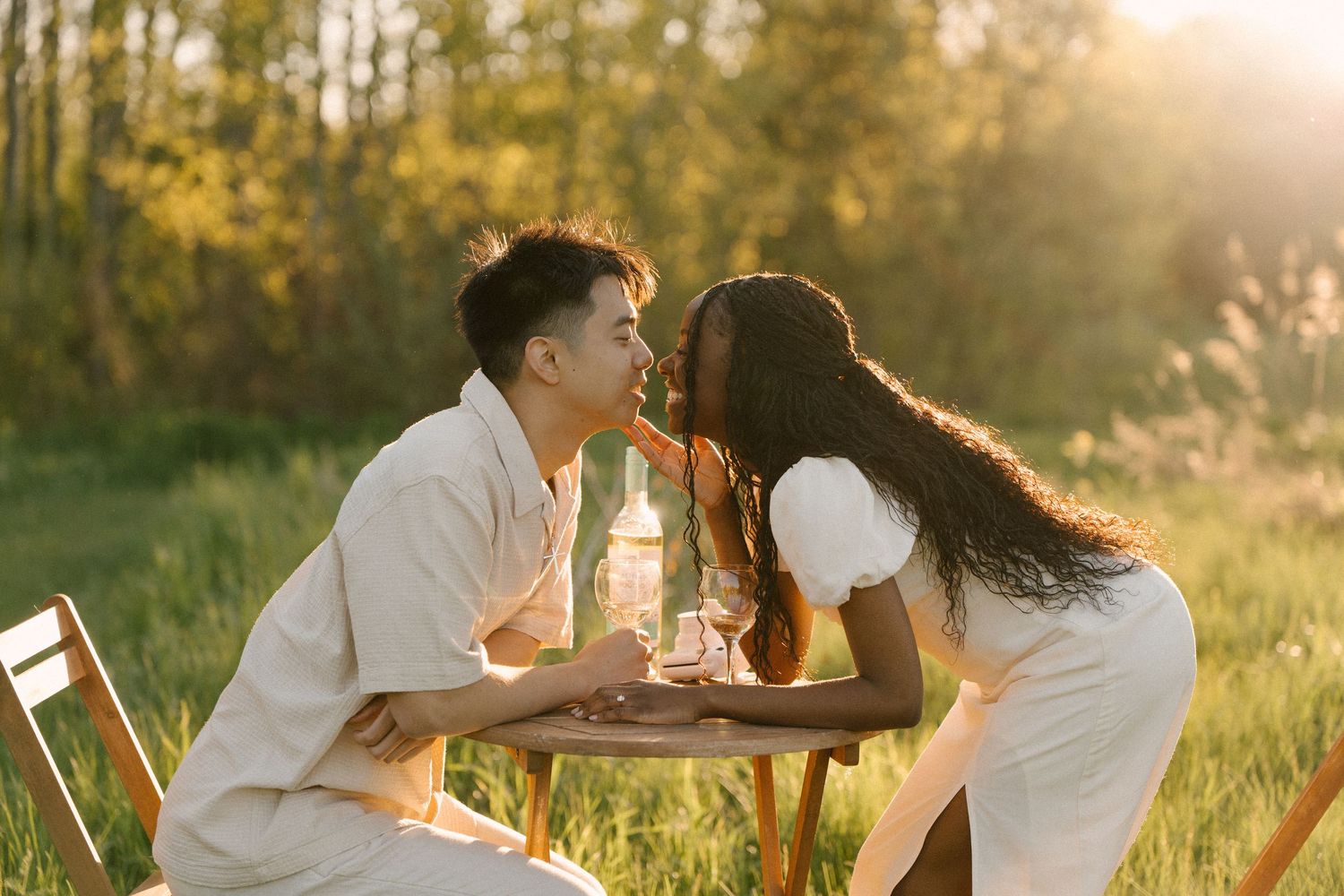 Couple sharing a romantic moment at an outdoor table surrounded by golden sunlight and lush greenery.