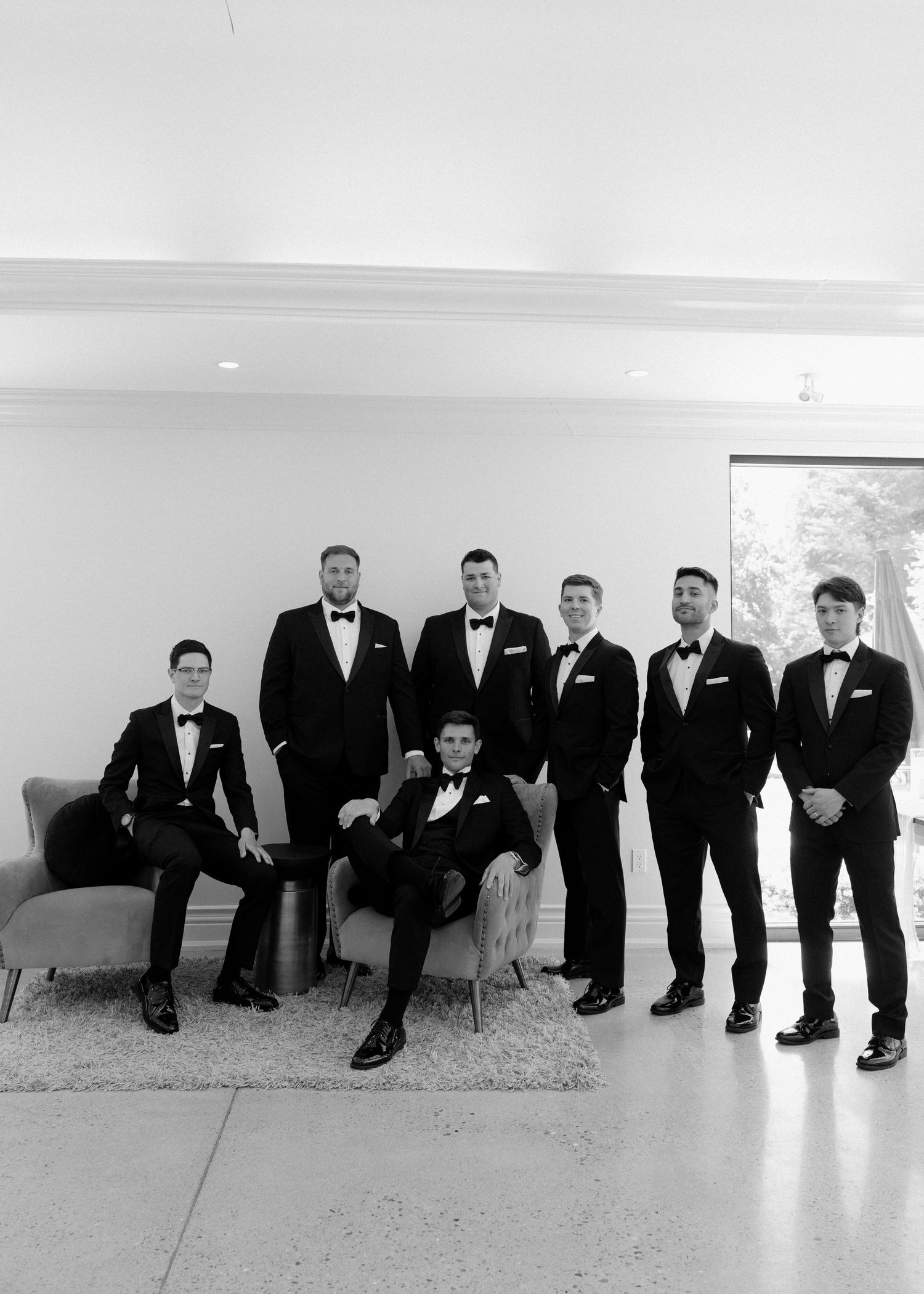 Groom and groomsmen posing in matching black tuxedos in elegant black and white wedding party portrait.