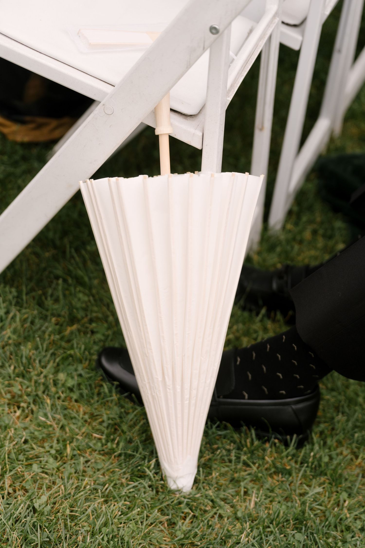 White folded paper fan program hanging on chair at outdoor wedding ceremony on green grass.
