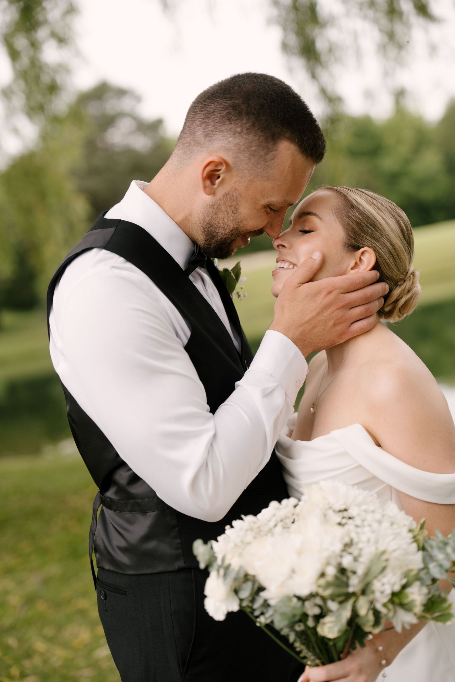Groom gently cups bride's face as they share a romantic moment outdoors on wedding day at Guelph golf club.