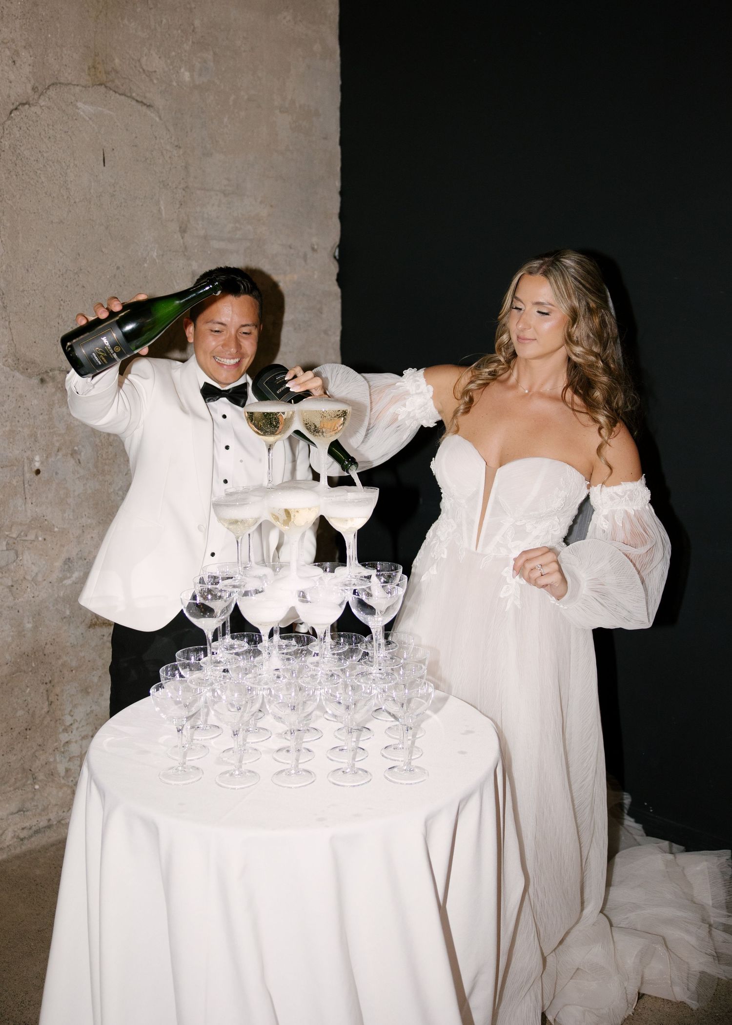 Bride and groom pouring champagne tower at elegant wedding reception celebration.
