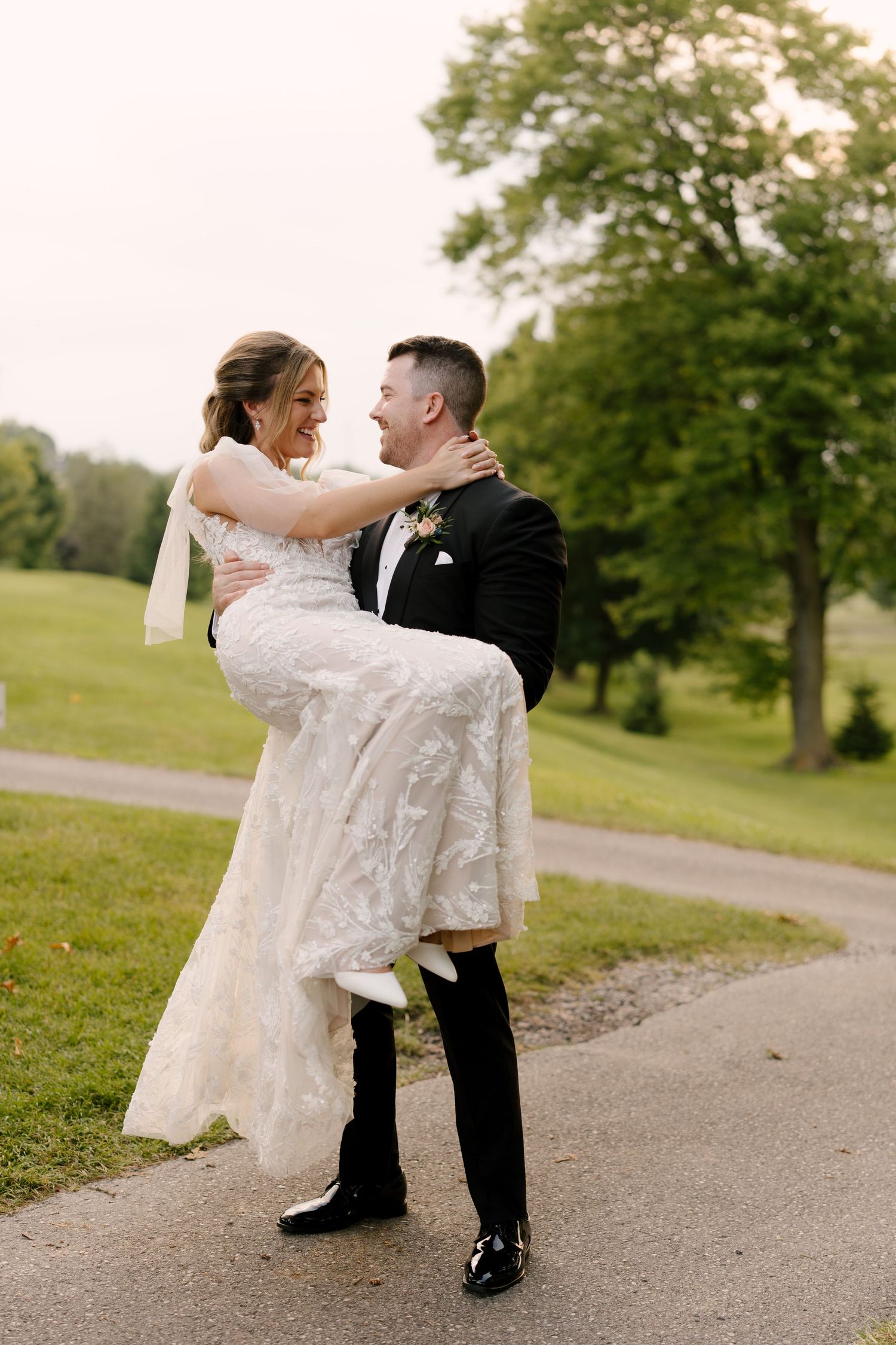 Smiling groom lifting his bride in a white lace gown on a garden path at their wedding.