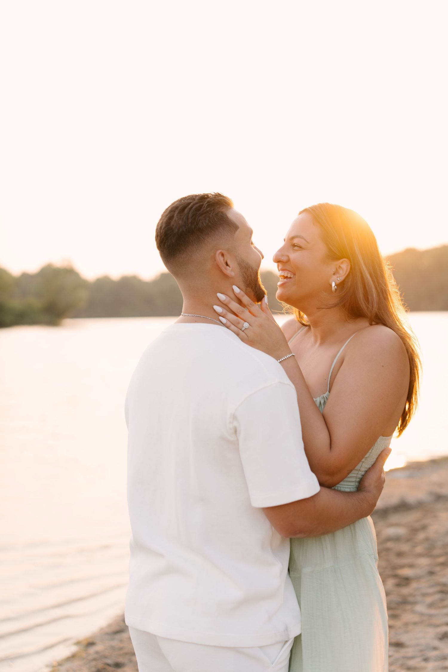Happy couple embracing on sandy beach during golden sunset by the water.