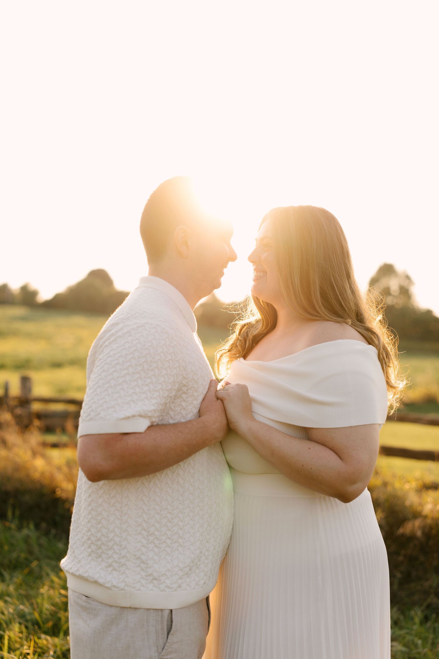 Couple nearly kissing backlit by bright golden sunset in a scenic field.