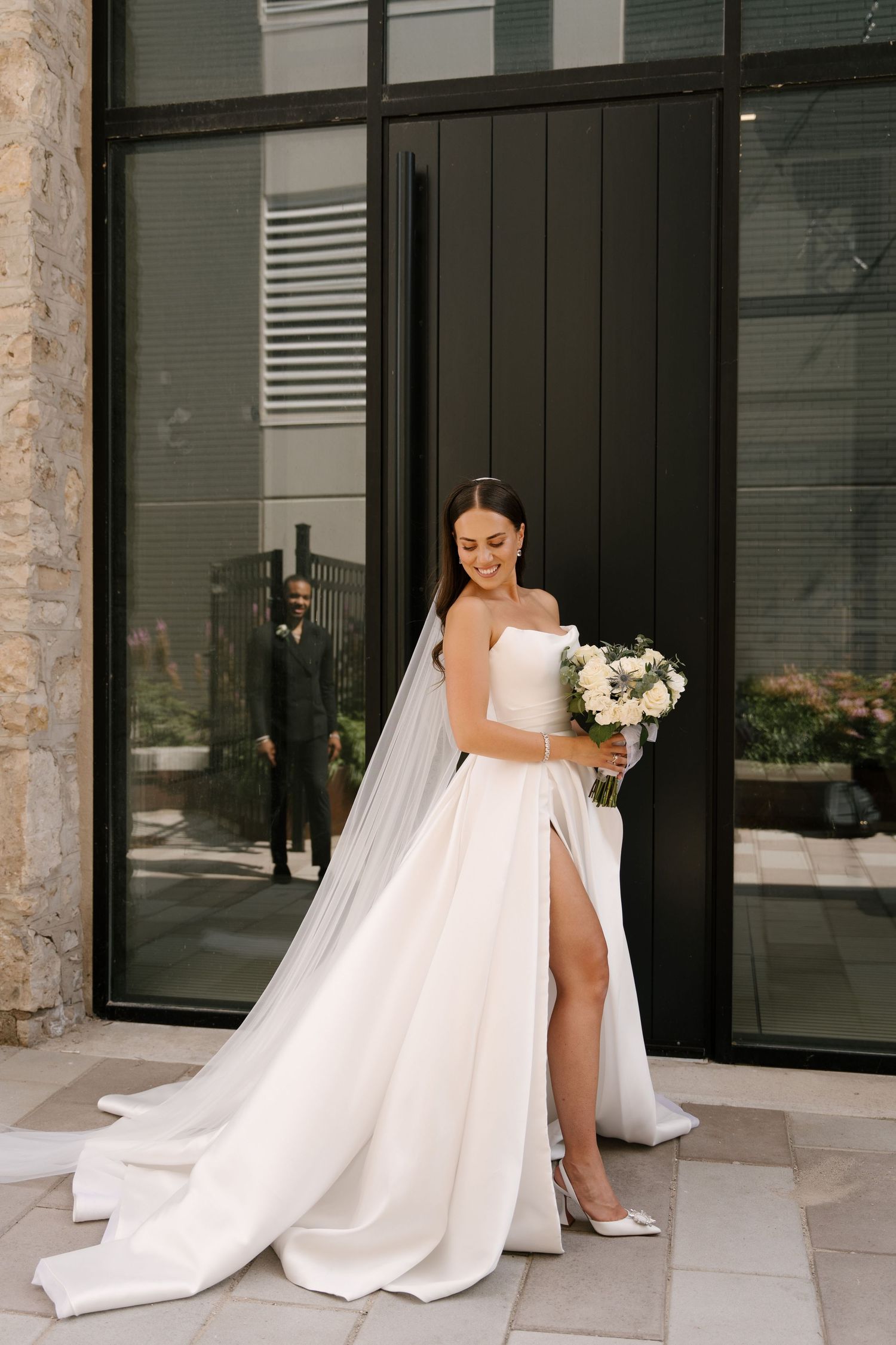 Elegant bride in a strapless white gown with a high slit holds a bouquet outside a modern Tapestry Hall venue.