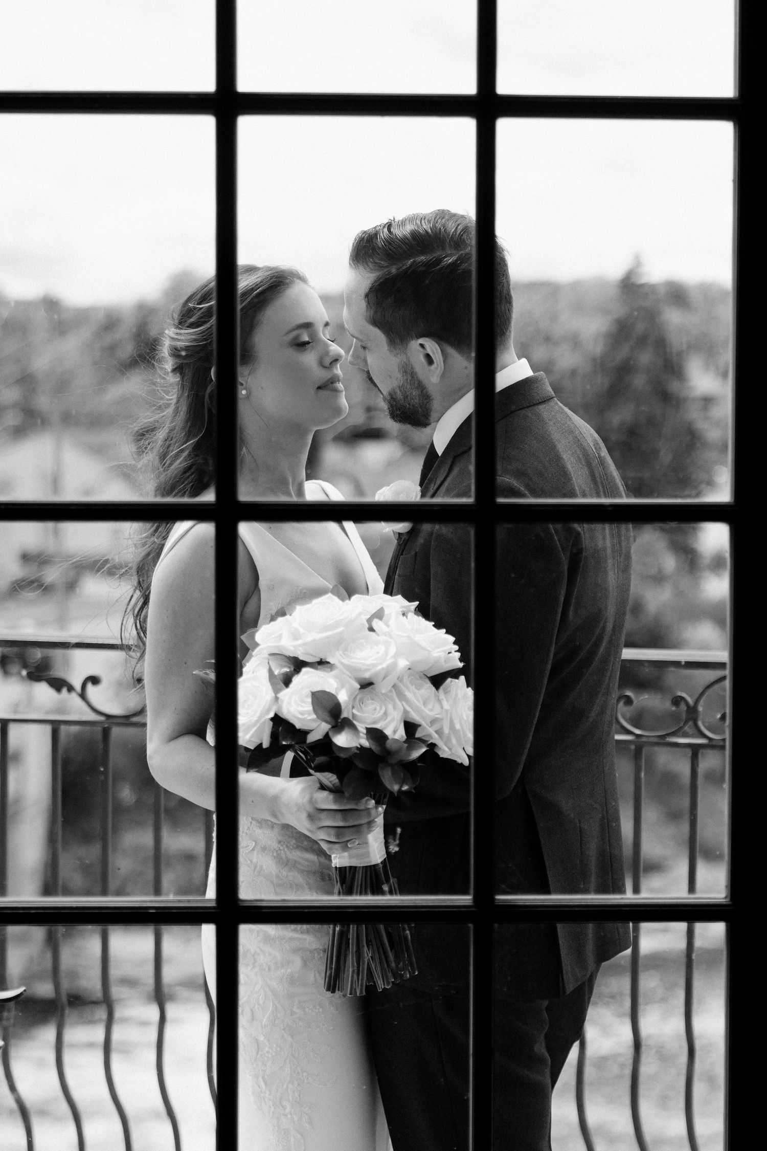 Black and white romantic portrait of bride and groom nearly kissing through decorative window panes at Cambridge Mill.