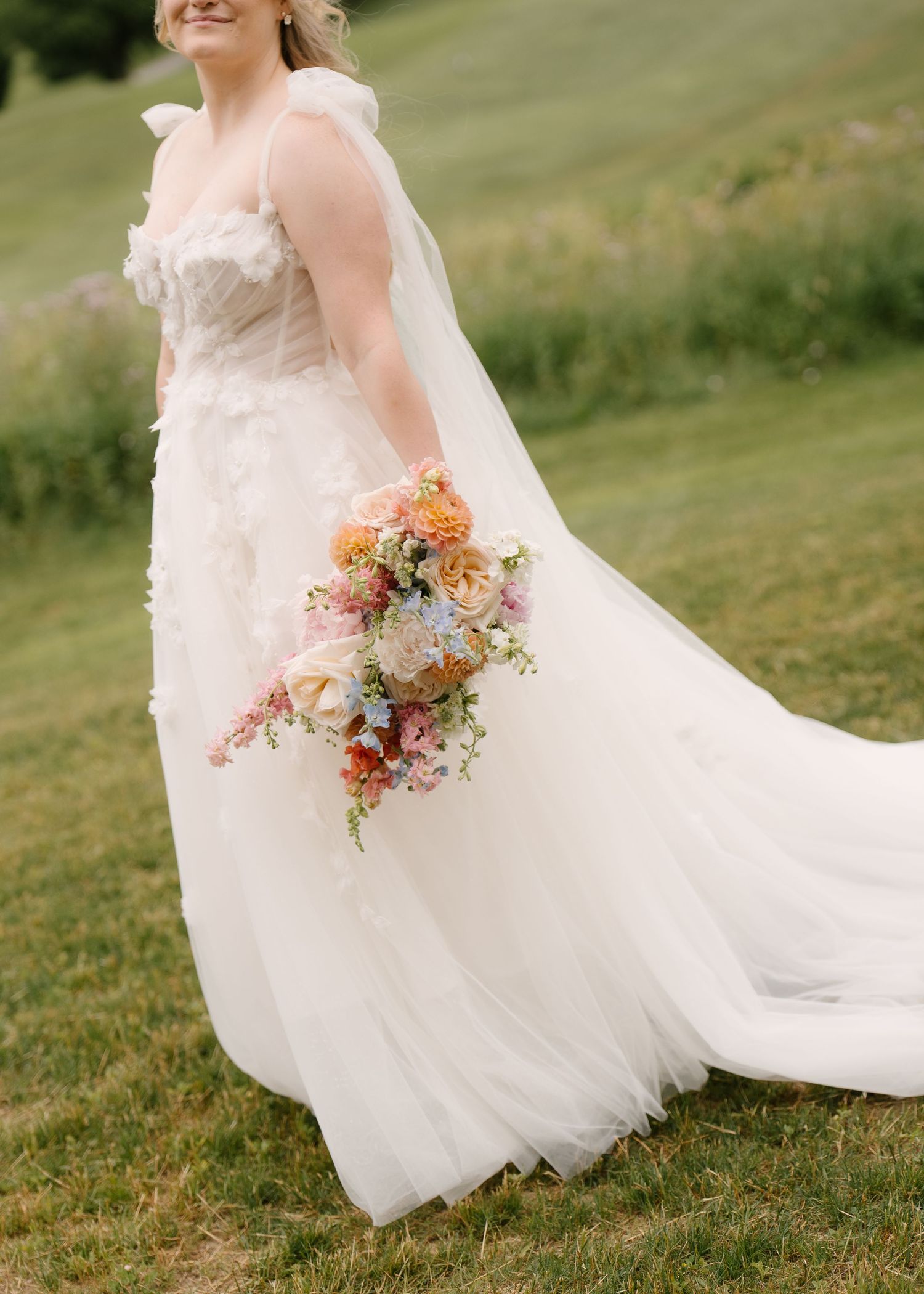 Bride in floral tulle gown holds a colourful pastel bouquet on a green hillside at St Marys Golf Club.