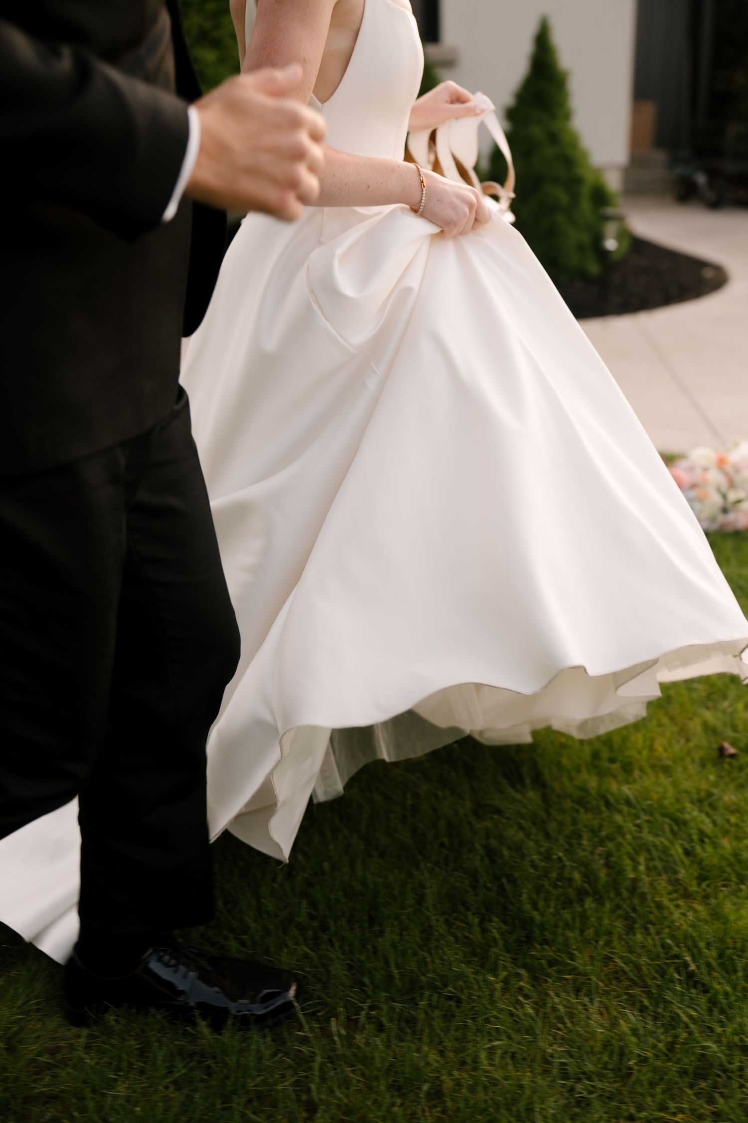 Bride in white gown and groom in black tuxedo dancing on green grass at outdoor wedding ceremony.