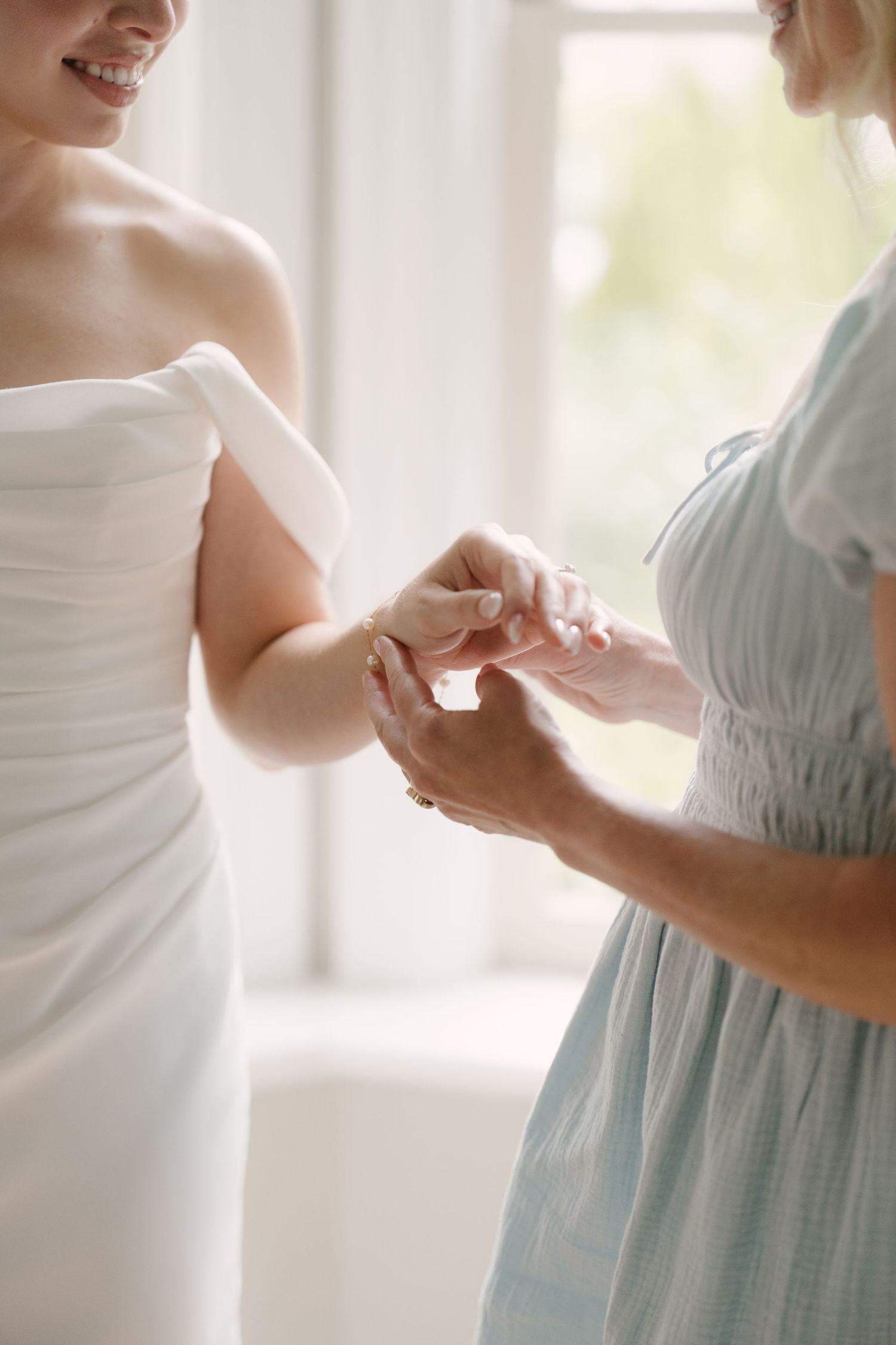 Close-up of bridesmaid helping bride put on delicate gold bracelet before wedding.