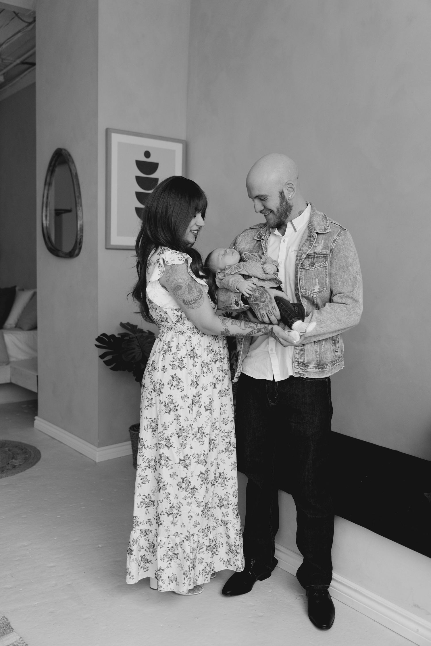 Black and white portrait of tattooed couple standing and holding their newborn baby in modern home.