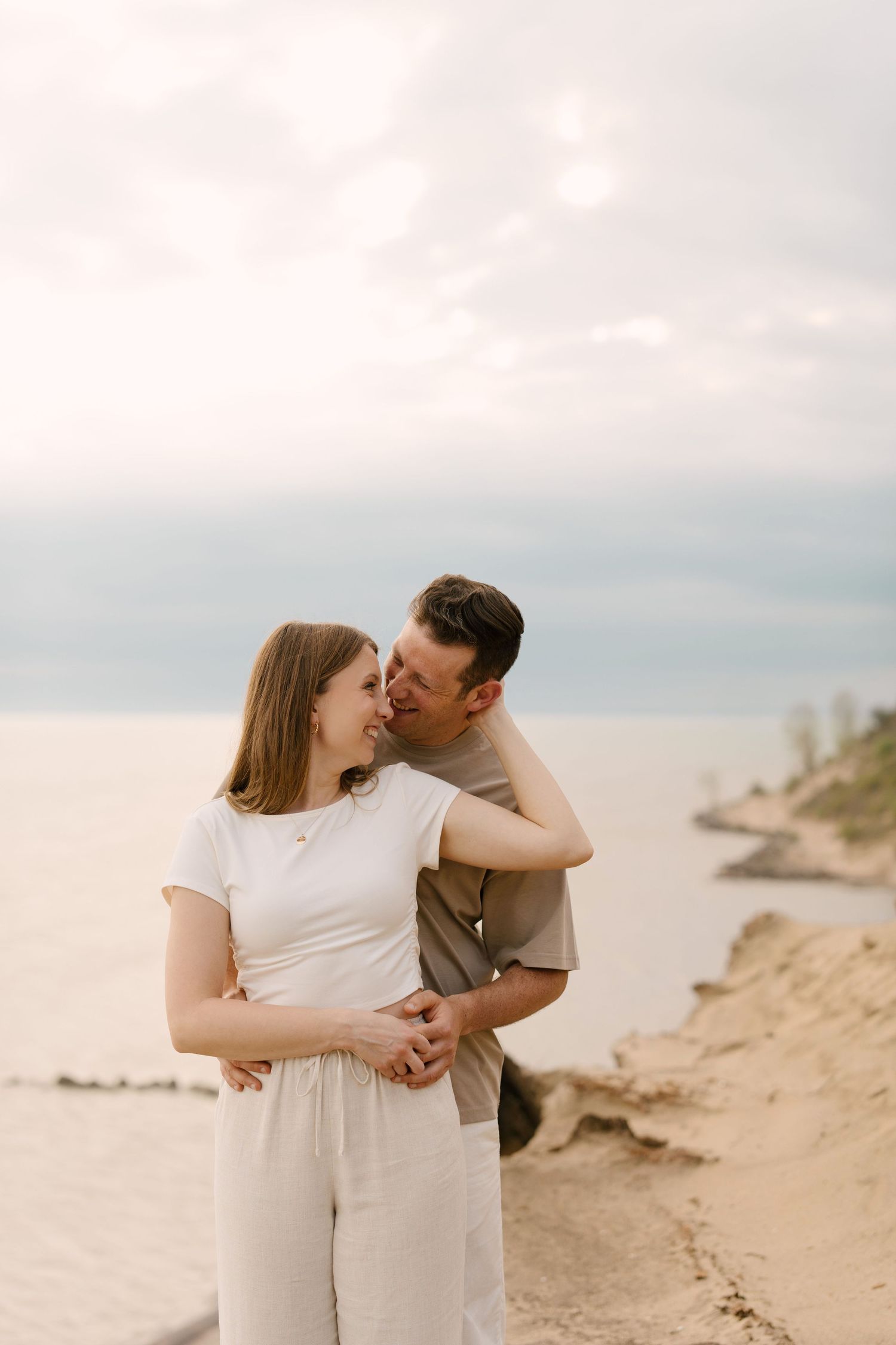 Romantic couple holding hands and gazing at each other on a sandy lakeside bluff.