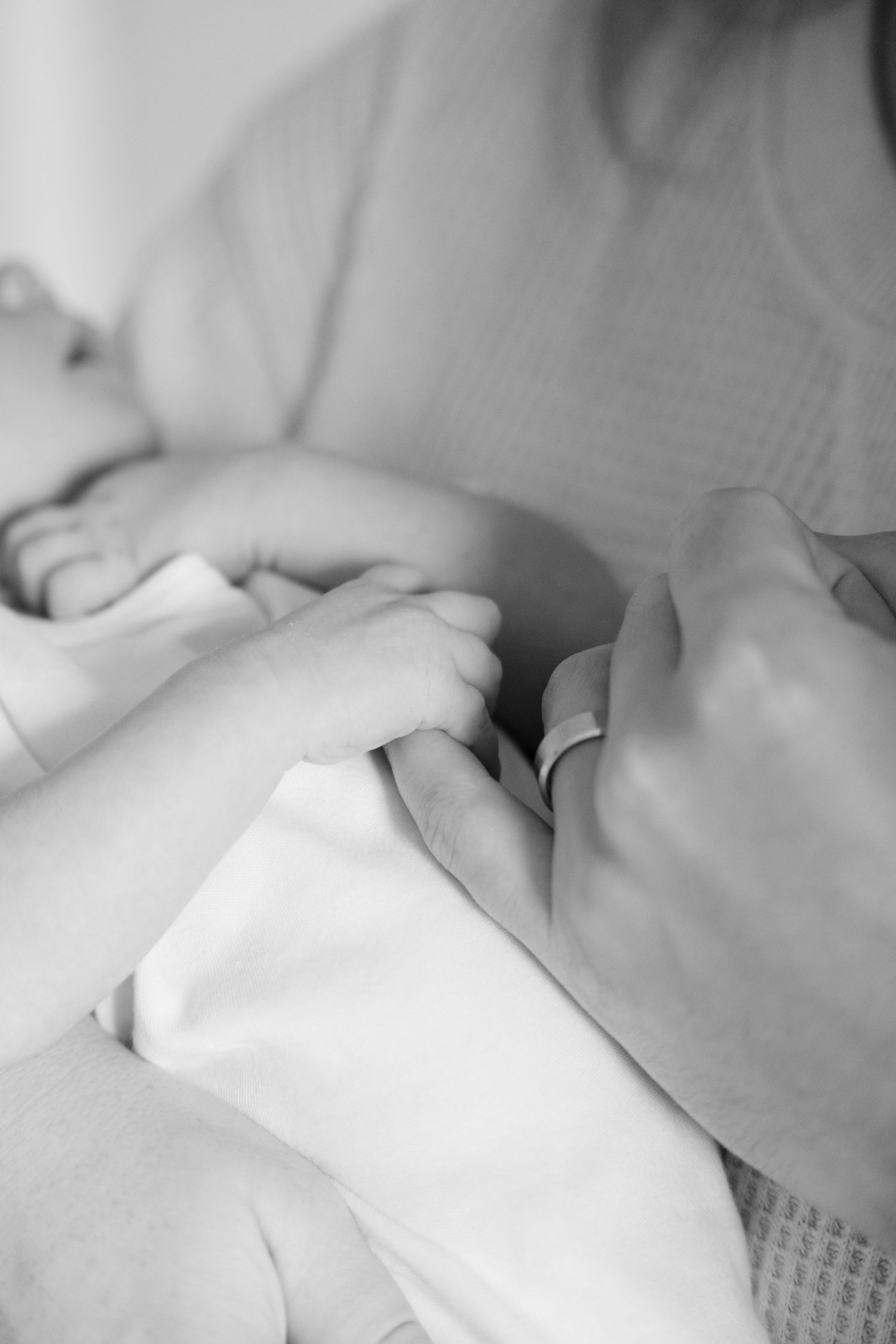 Black and white close-up of newborn baby fingers gently holding mothers hand.