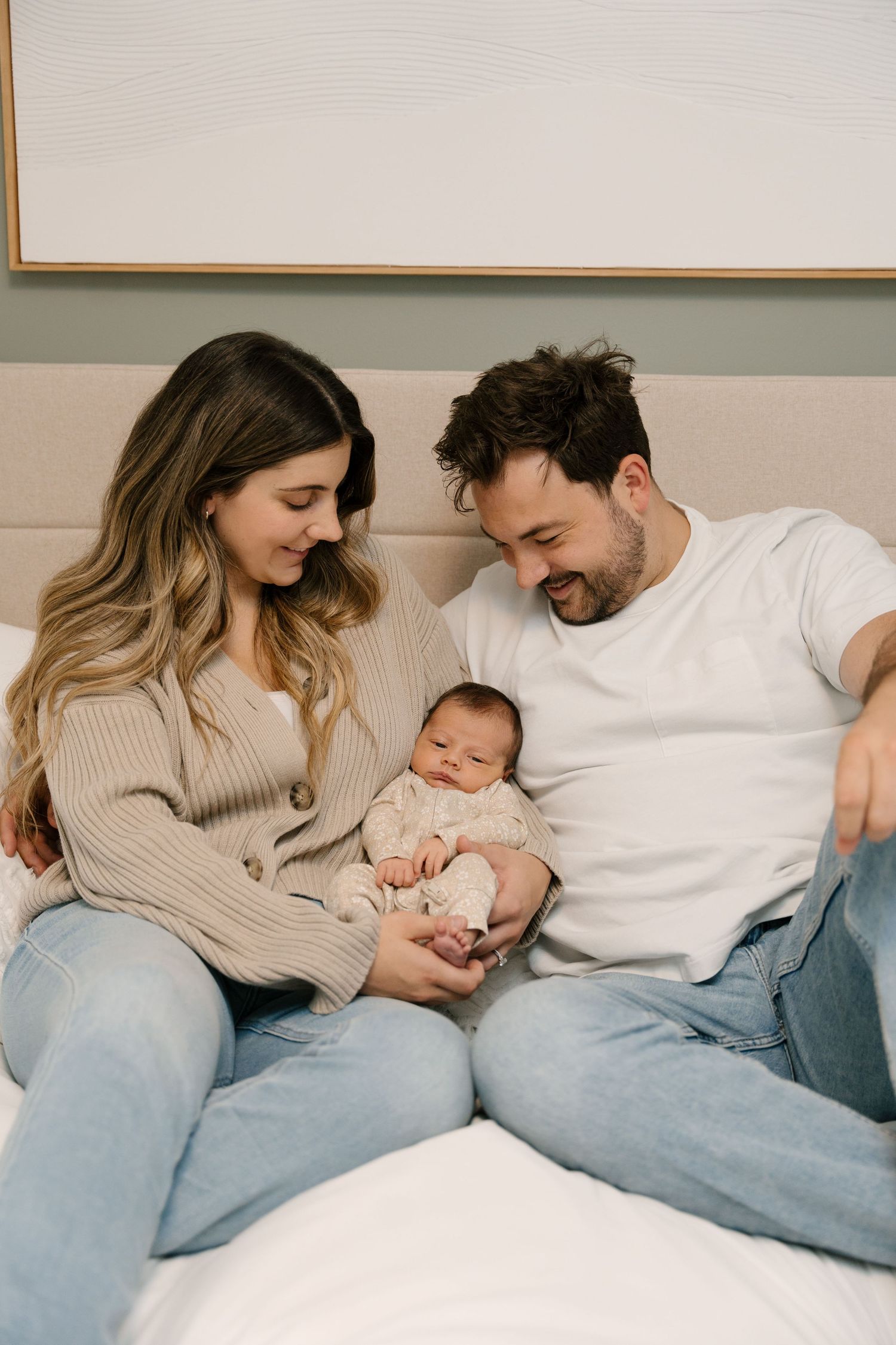 Happy young parents sitting on bed smiling at their newborn baby, enjoying a tender family moment at home.