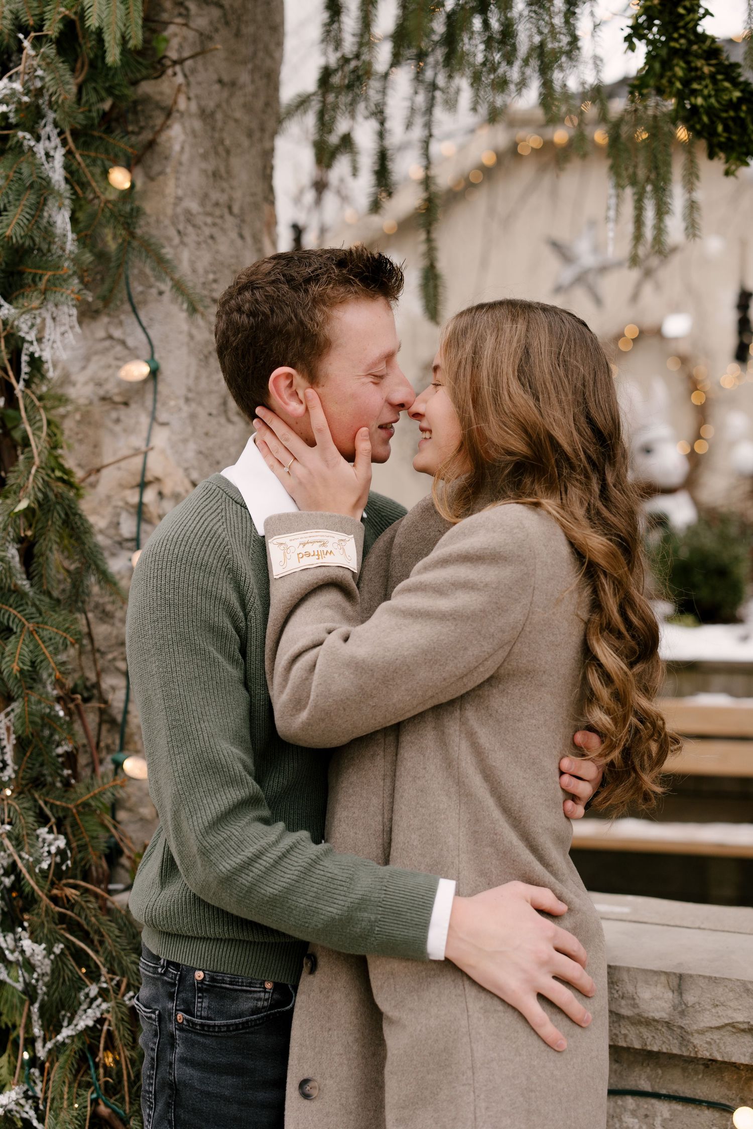 A joyful couple shares a tender moment outdoors surrounded by snow-dusted pine branches.
