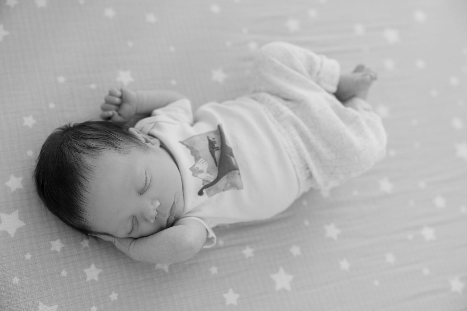 Peaceful newborn baby sleeping on a star-patterned blanket in black and white photo.