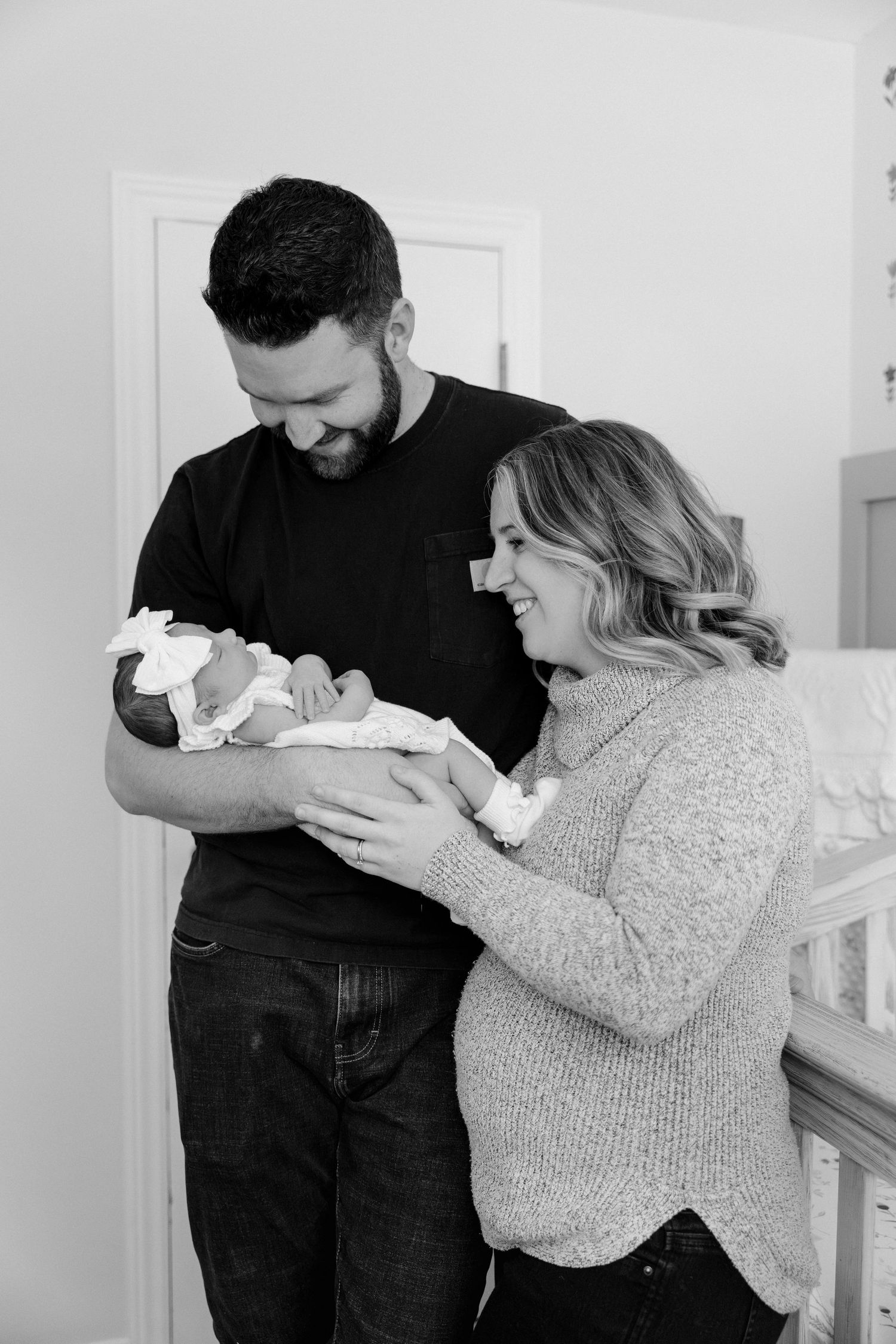 Black and white photo of smiling new parents holding their newborn baby girl in nursery.